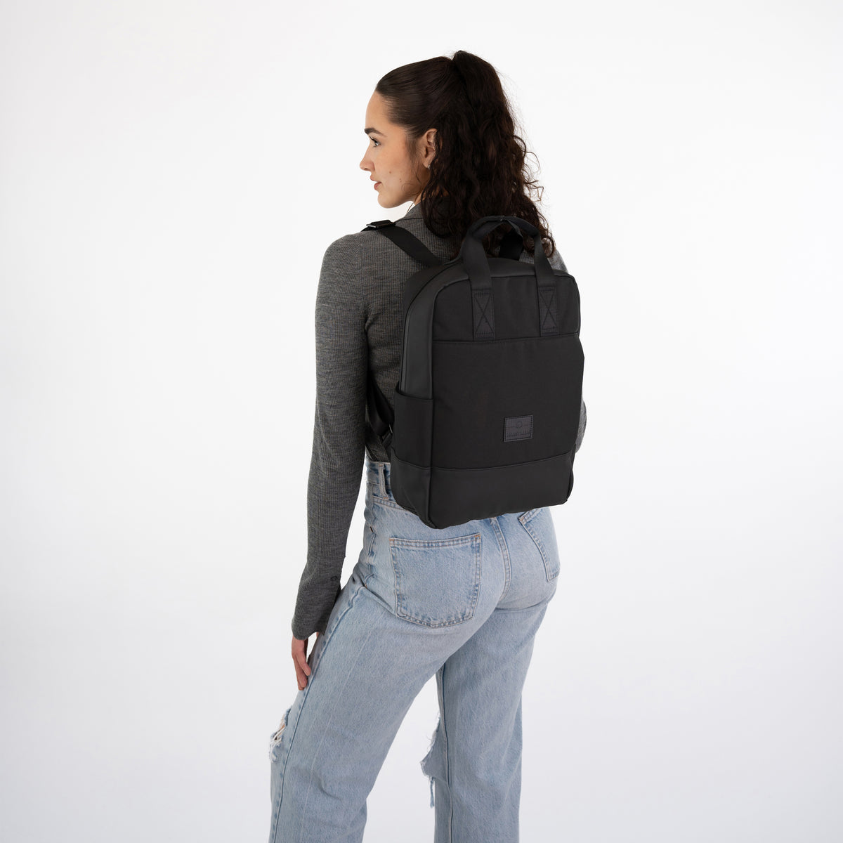 Frau mit schwarzem Johnny Urban Rucksack 'Jona Medium' trägt grauen Pullover und helle Jeans
