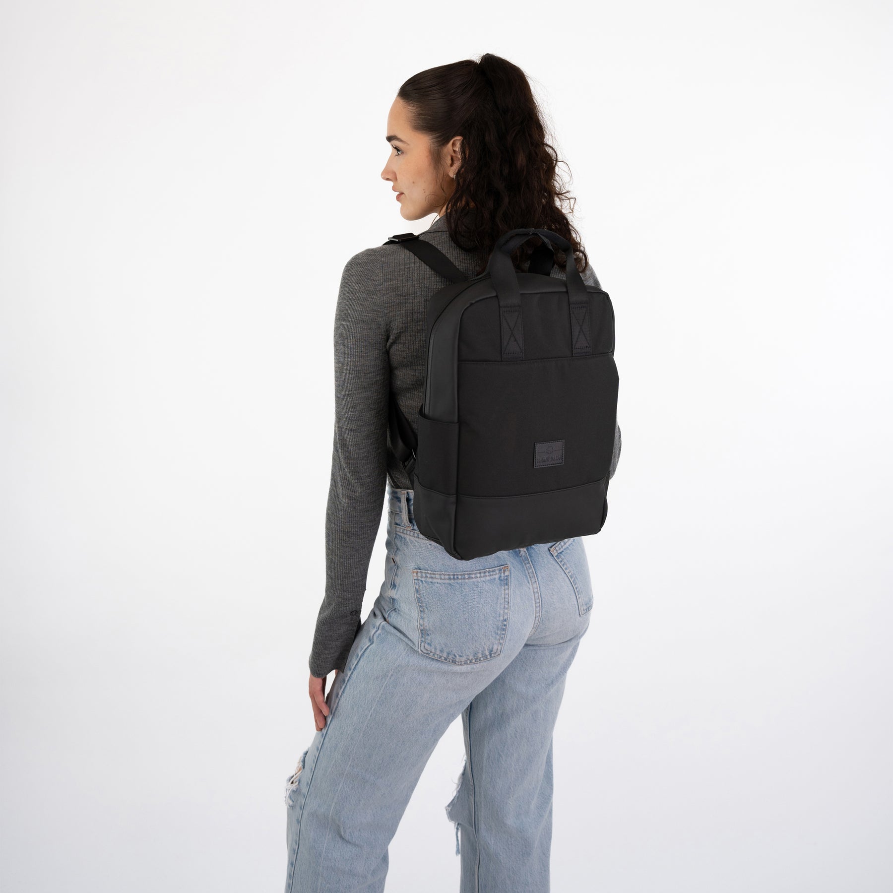 Frau mit schwarzem Johnny Urban Rucksack 'Jona Medium' trägt grauen Pullover und helle Jeans