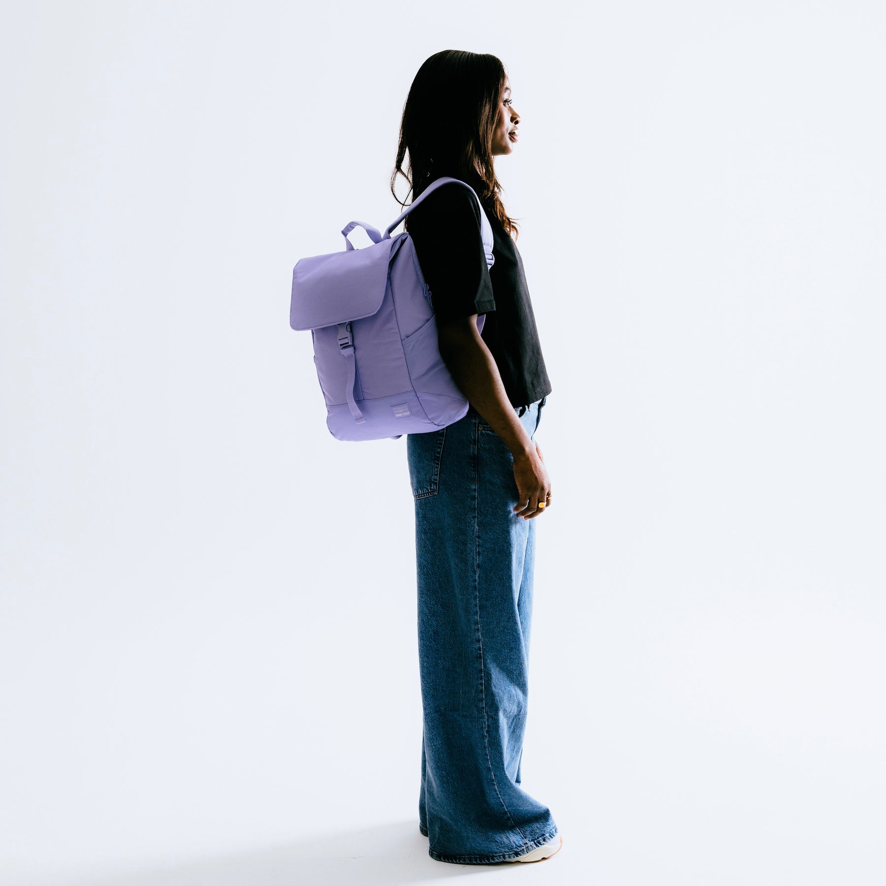 Frau trägt lila Rucksack 'Mika', steht seitlich in schwarzem T-Shirt und weitem Jeansrock