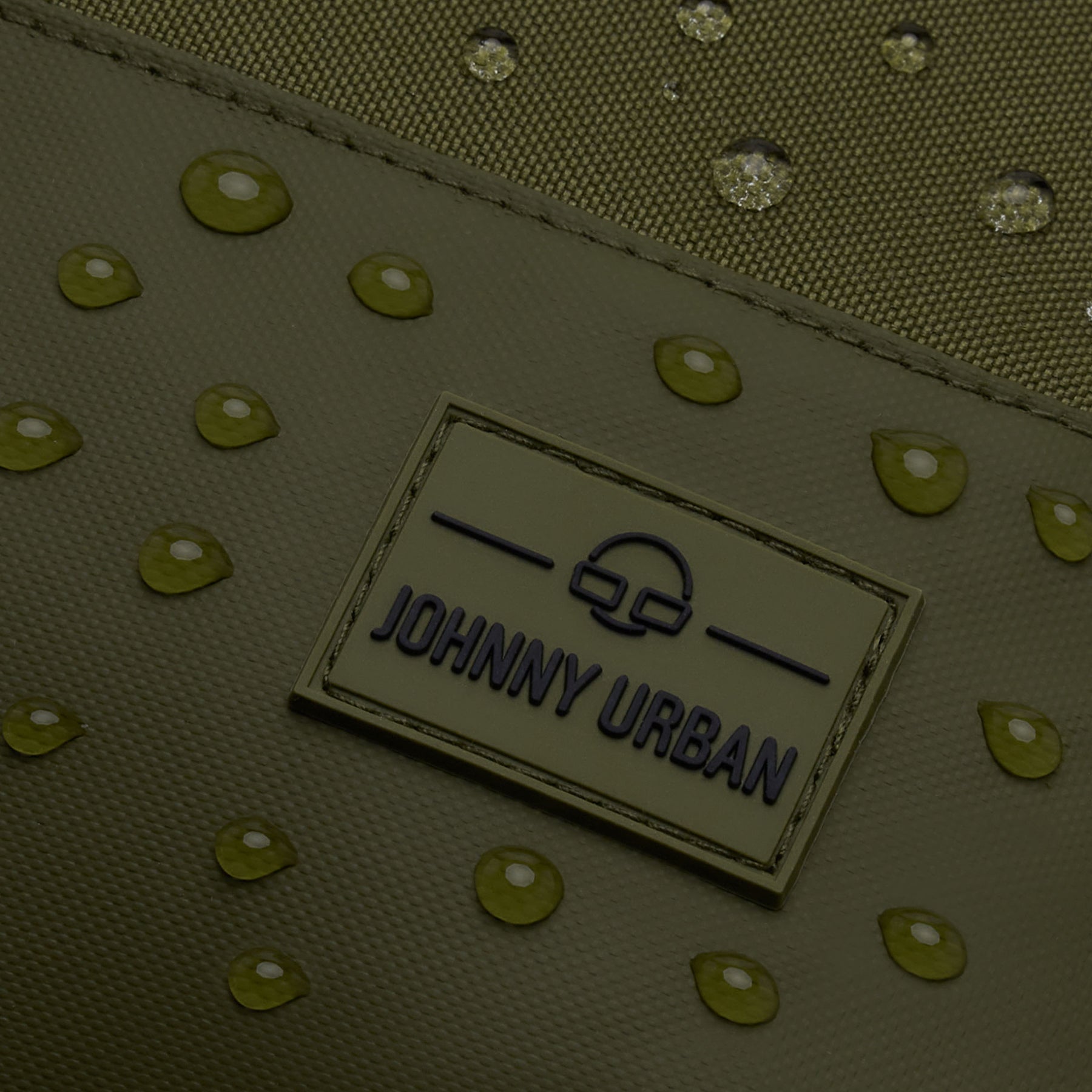 Nahaufnahme des wasserabweisenden, olivfarbenen Rucksacks 'Mika' von Johnny Urban mit Markenlogo und Wassertropfen