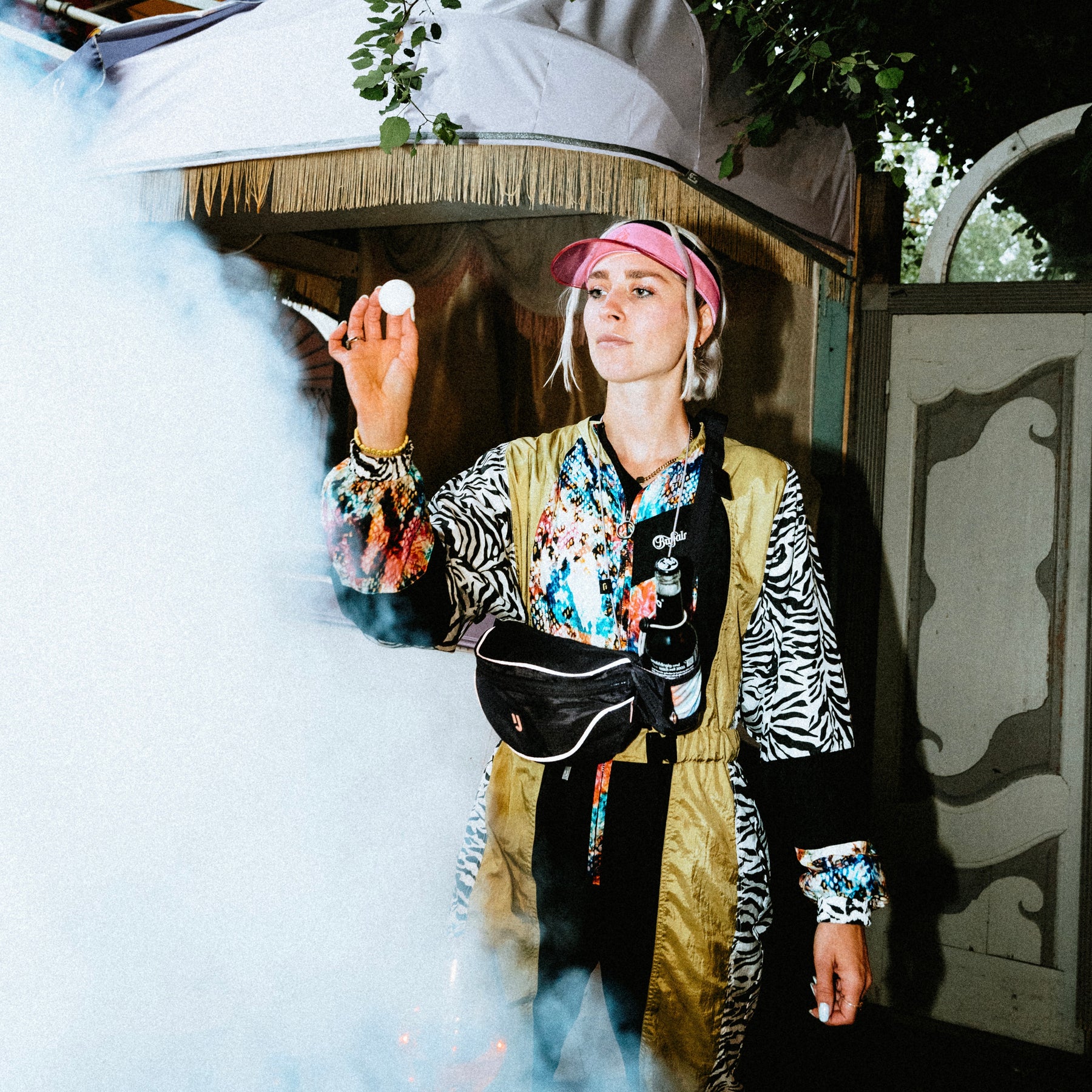 Frau mit bunter Jacke und rosa Cap trägt die Johnny Urban 2in1 Bauchtasche 'Jimmy' in Schwarz und hält ein kleines weißes Objekt