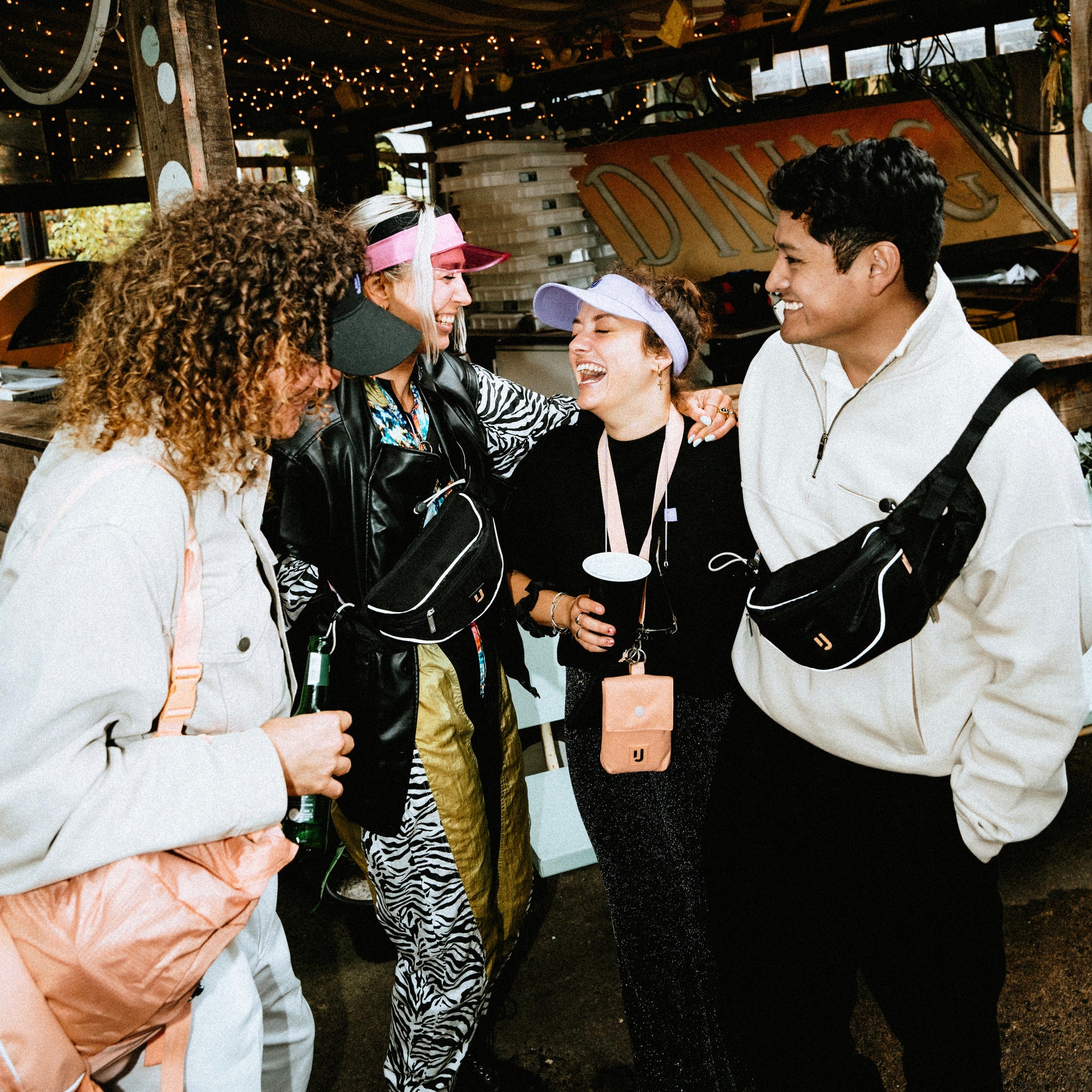 Vier Personen lachend bei einem Festival, zwei tragen die schwarze 2in1 Bauchtasche 'Jimmy' von Johnny Urban
