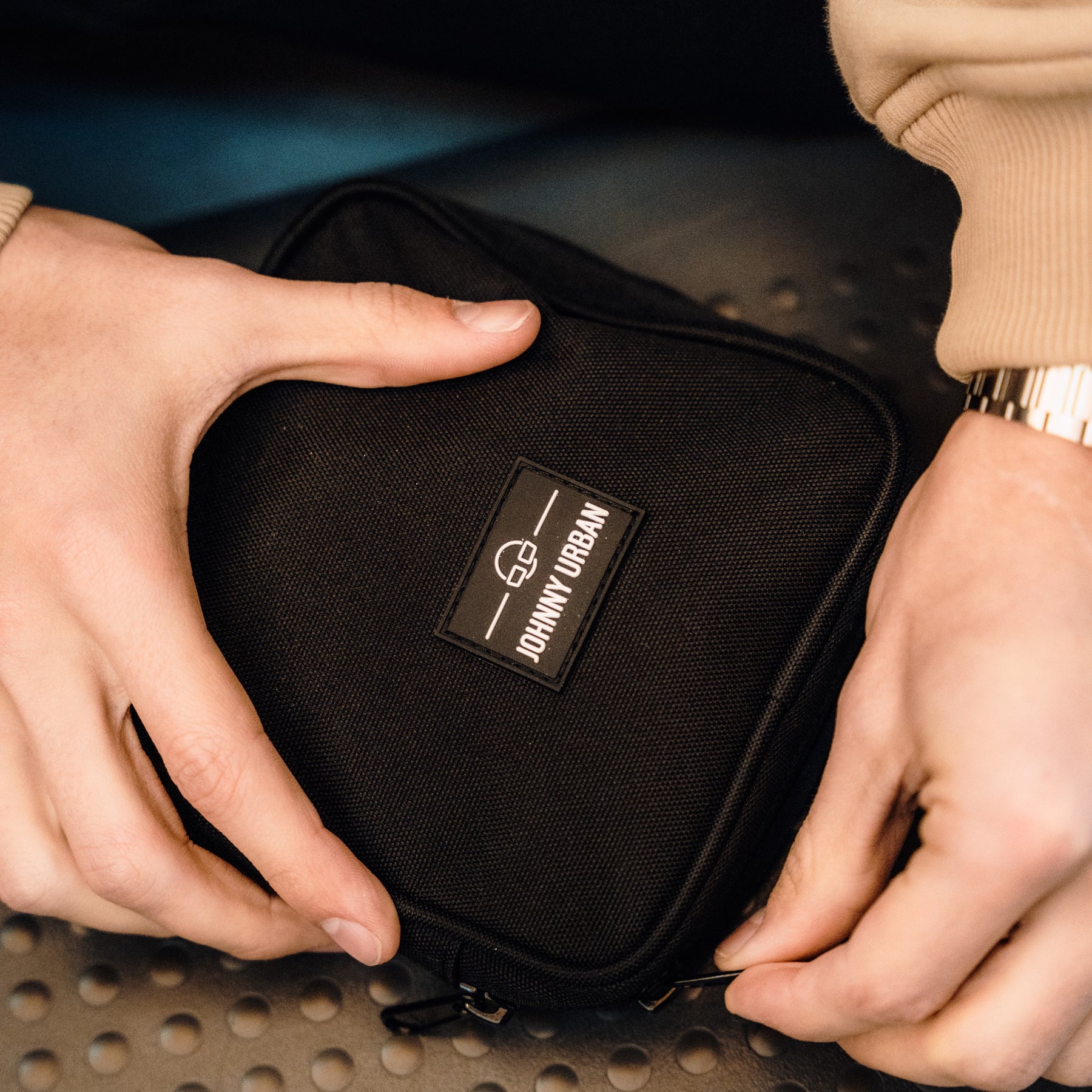 Schwarzer Tech Organizer 'Ted' von Johnny Urban in rechteckiger Form aus robustem Material, gehalten von zwei Händen