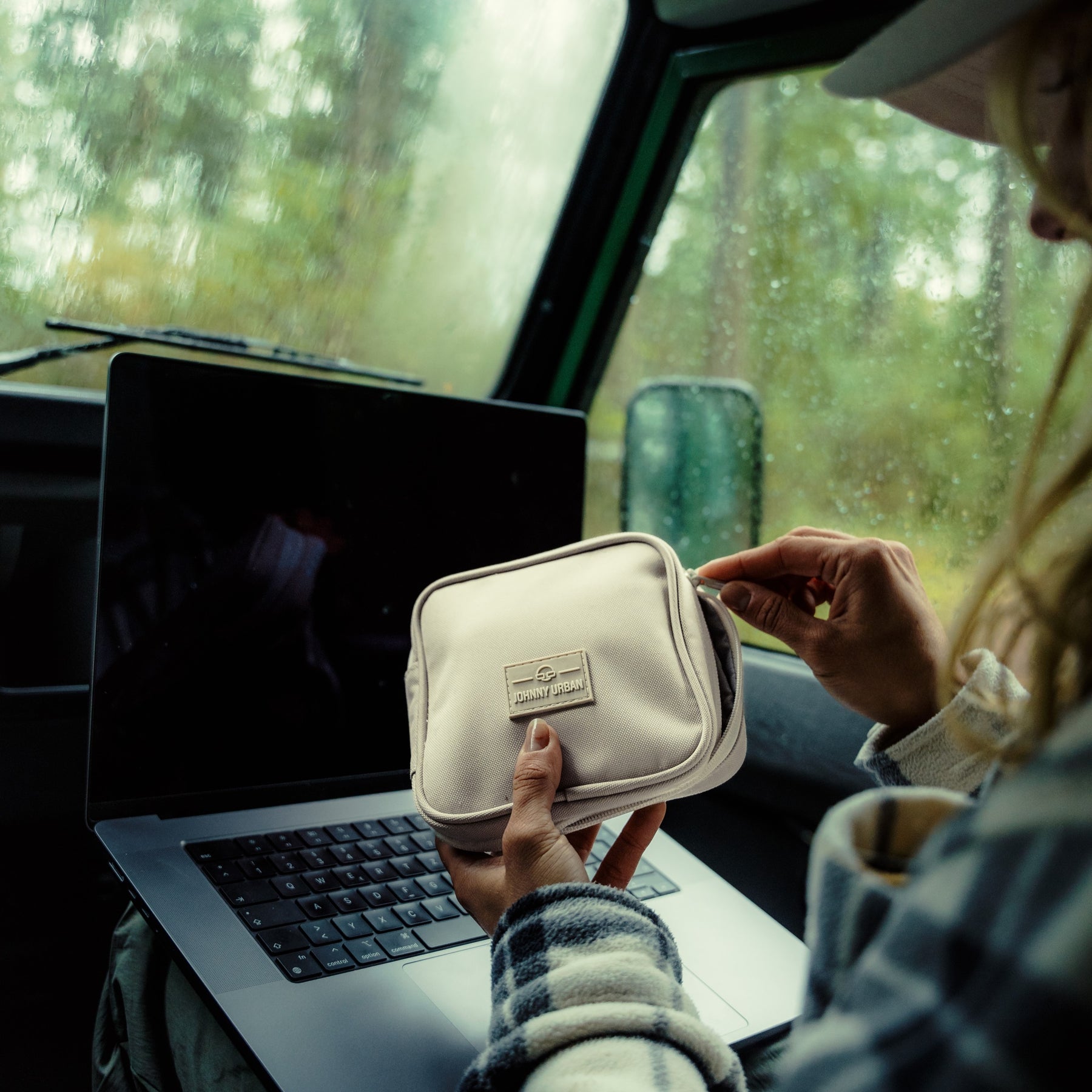 Beige Tech Organizer 'Ted' von Johnny Urban in Händen vor einem Laptop im Auto bei Regen
