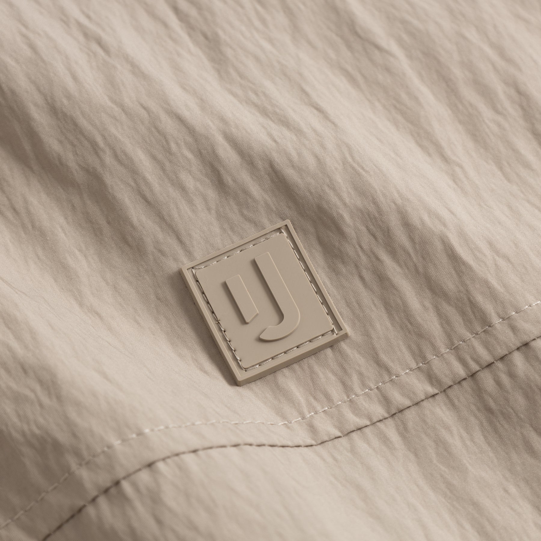 Nahe Aufnahme des Logos auf der beigen Übergangsjacke 'Lennon' von Johnny Urban