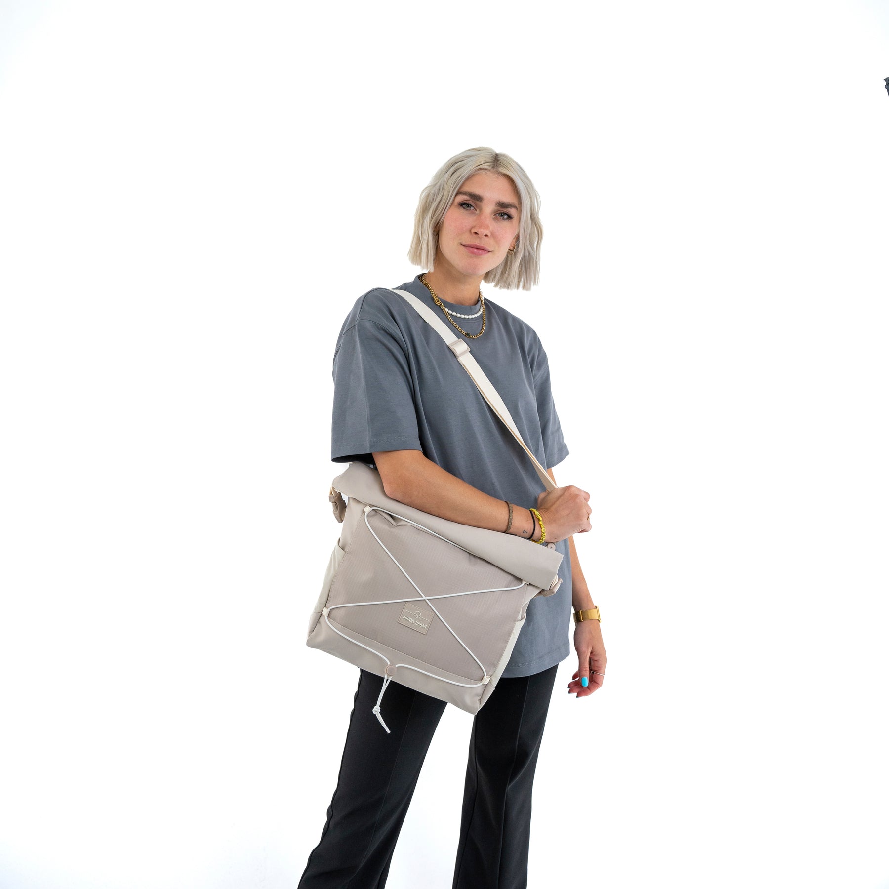 Frau mit kurzer blonder Haare trägt beige Umhängetasche 'Dylan' von Johnny Urban, graues T-Shirt, schwarze Hose