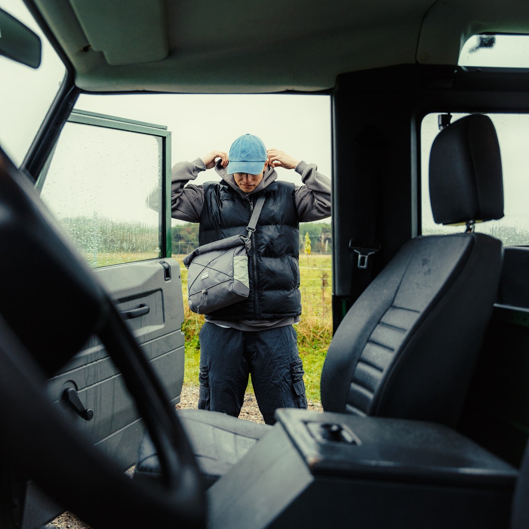 Mann trägt graue Umhängetasche 'Dylan' von Johnny Urban, steht vor offenem Autotür bei bewölktem Wetter