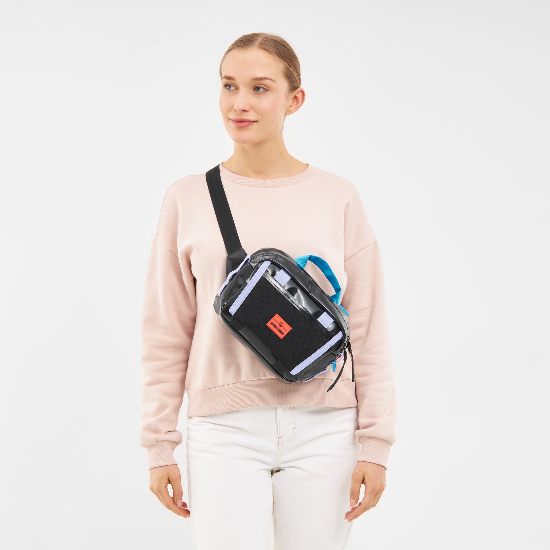 Frau trägt beigefarbenen Pullover und weiße Hose mit schwarzer, blauer und grauer Lenkertasche 'Nelson' quer am Oberkörper