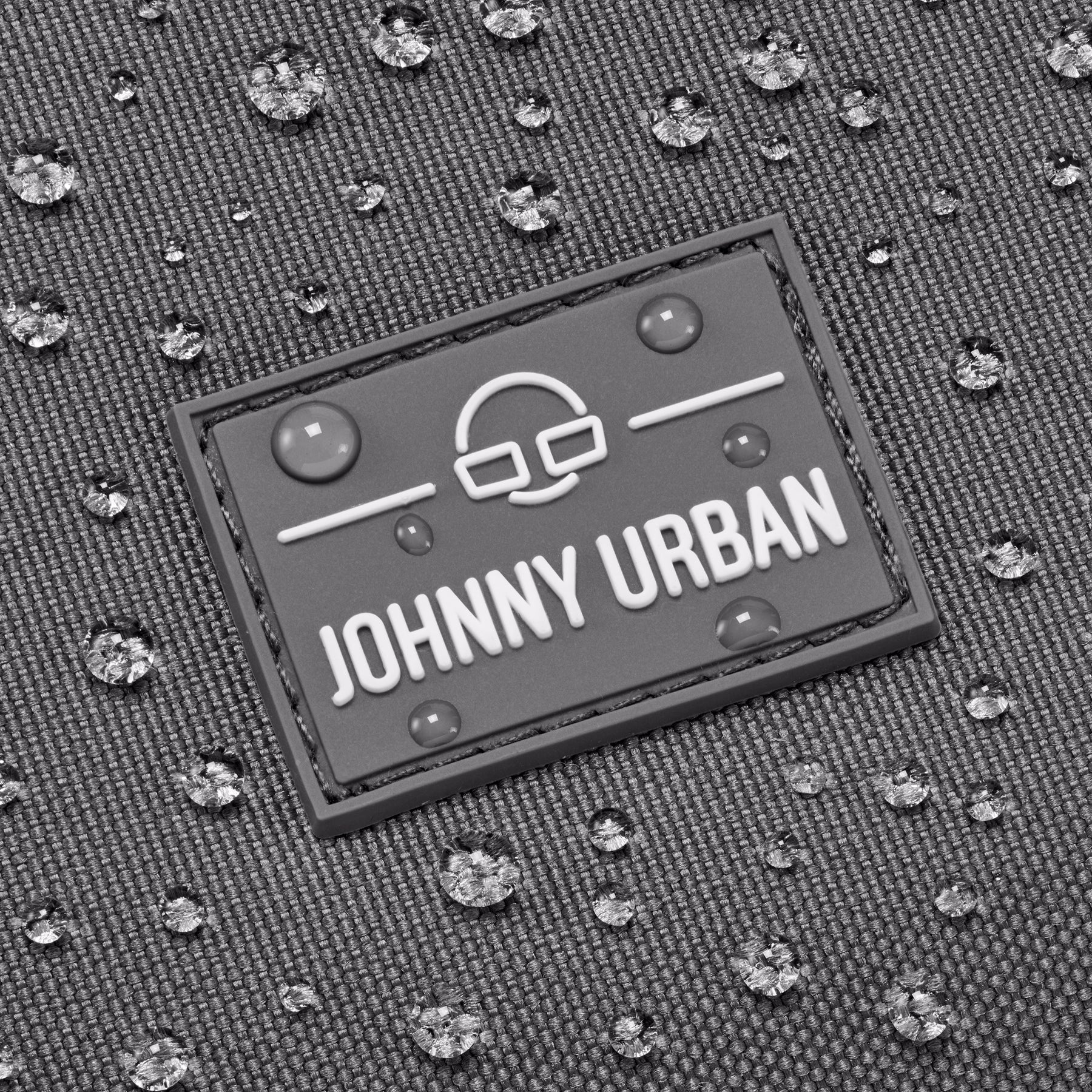 Nahaufnahme des Johnny Urban Logos auf wasserabweisendem, dunkelgrauem Stoff mit Wassertropfen