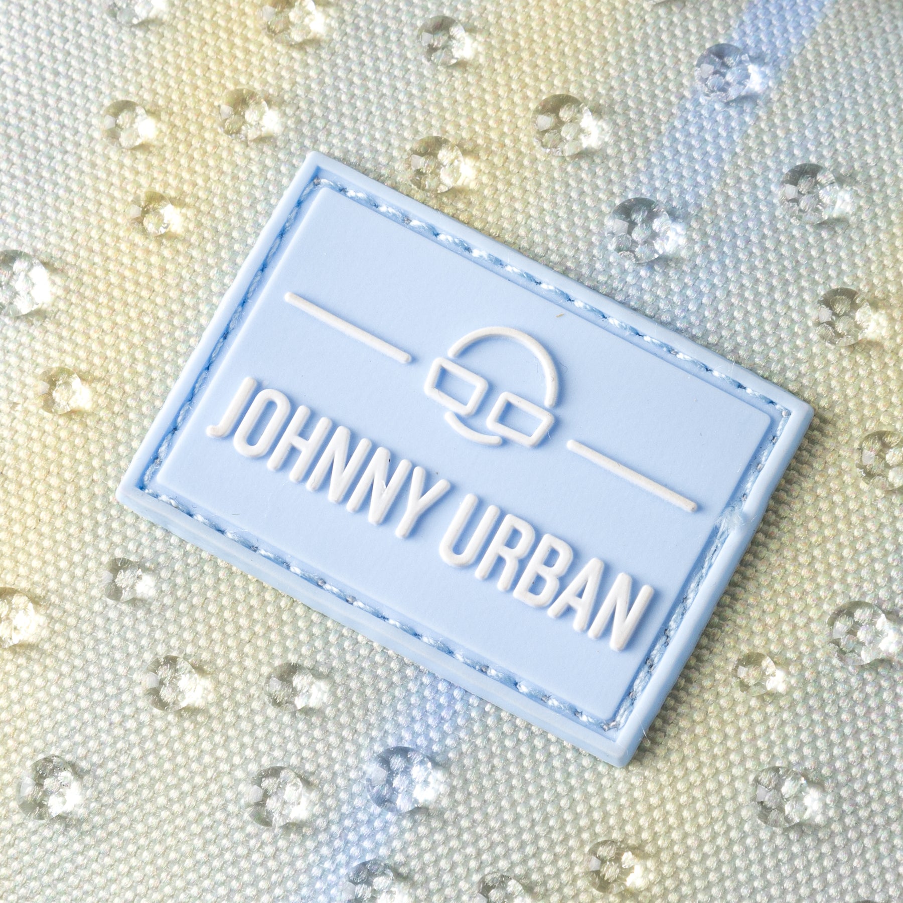 Johnny Urban Logo auf wasserabweisendem lilafarbenem Taschenstoff mit Wassertropfen
