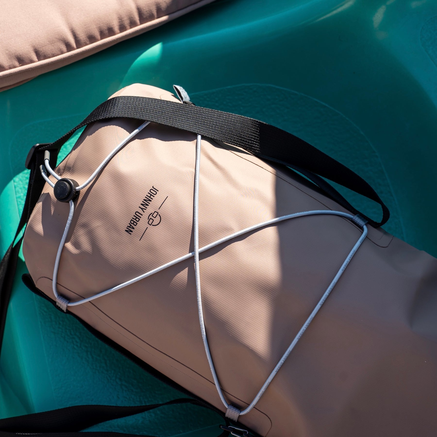 Beige wasserdichte Dry Bag 'Theo' von Johnny Urban mit schwarzem Schultergurt und elastischem Band, liegt in grünem Boot.