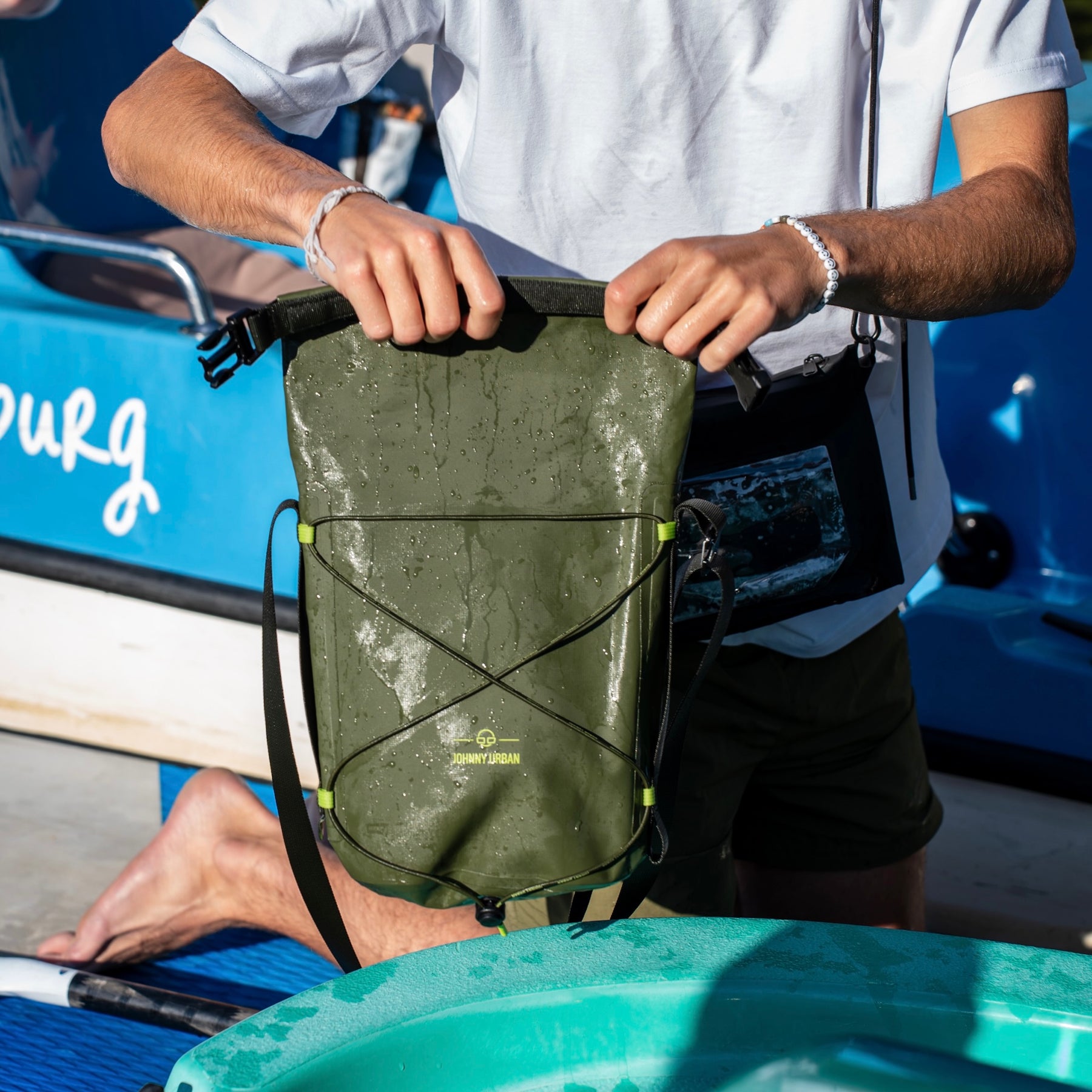 Olivegrüne wasserdichte Dry Bag 'Theo' von Johnny Urban mit nassen Tropfen, gehalten von einer Person in weißem T-Shirt