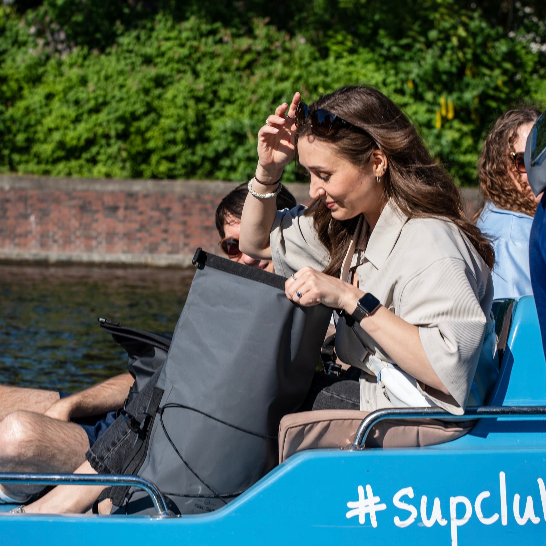 Frau auf Boot mit wasserdichtem Rolltop-Rucksack 'Myles' in Grau, öffnet ihn bei sonnigem Wetter