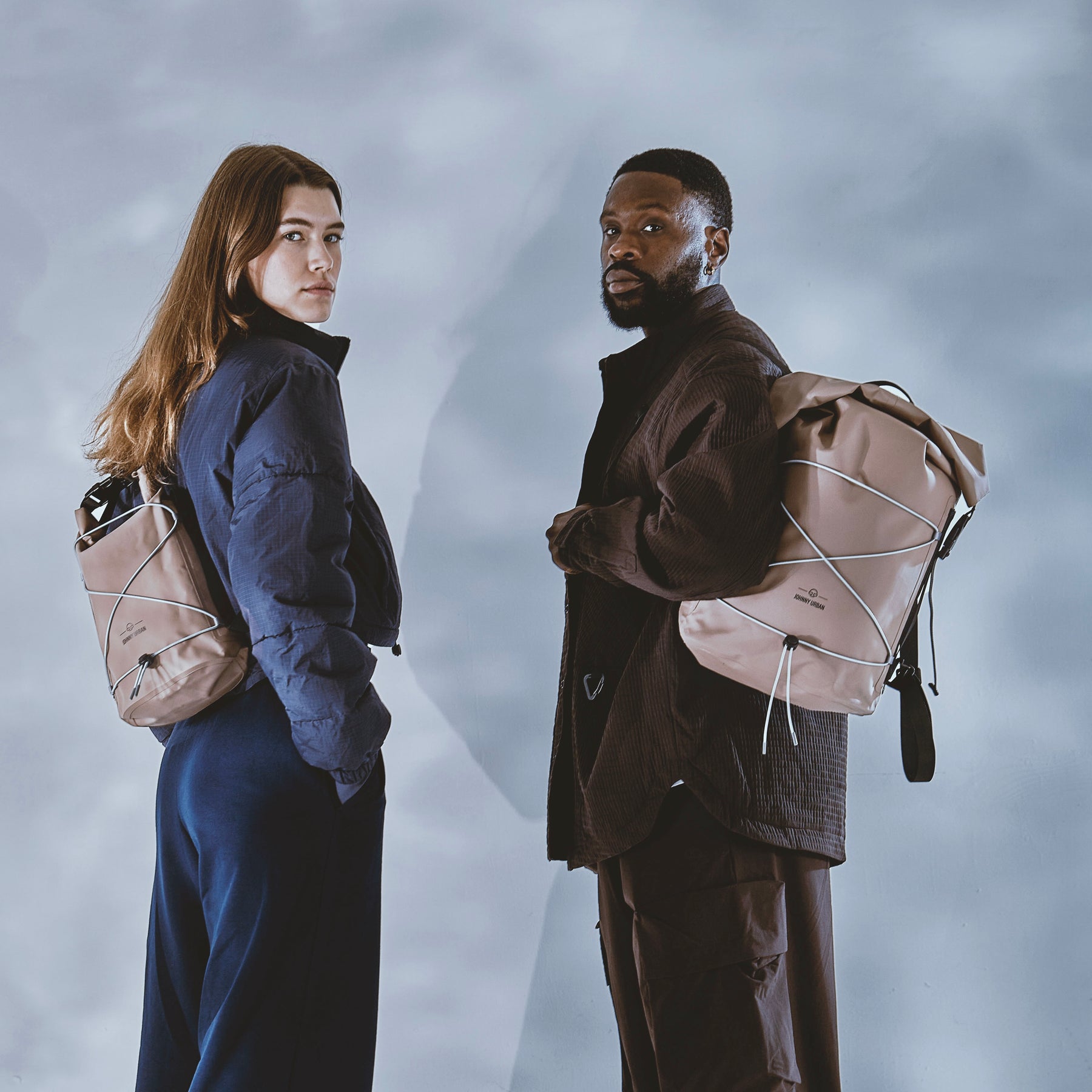 Frau und Mann tragen jeweils einen braunen Rolltop-Rucksack 'Myles' von Johnny Urban