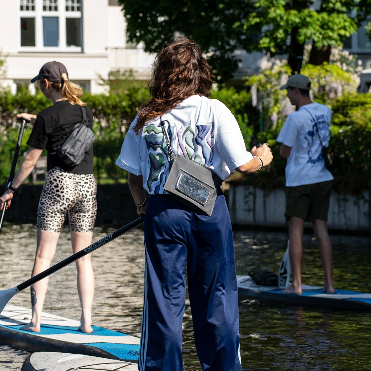 Drei Personen beim Stand-up-Paddling, eine trägt die schwarze Dry Bag 'Alfie' von Johnny Urban um die Hüfte
