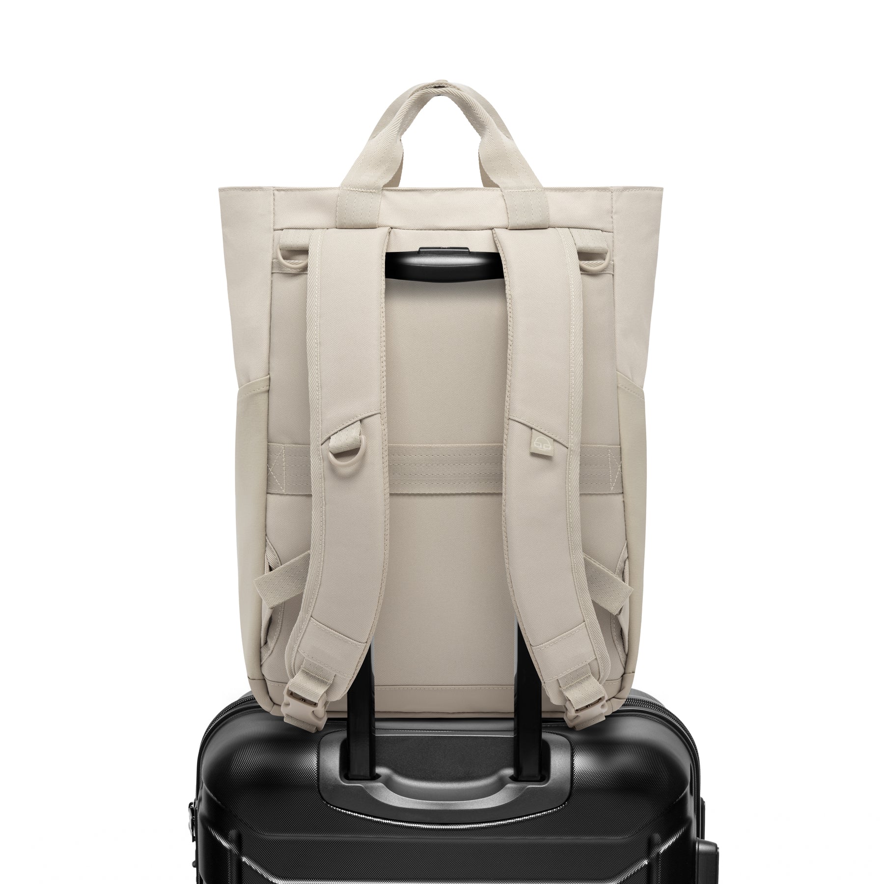 Rückseite der cremefarbenen Wickeltasche 'Blair' mit gepolsterten Trägern auf dem Griff eines schwarzen Reisekoffers