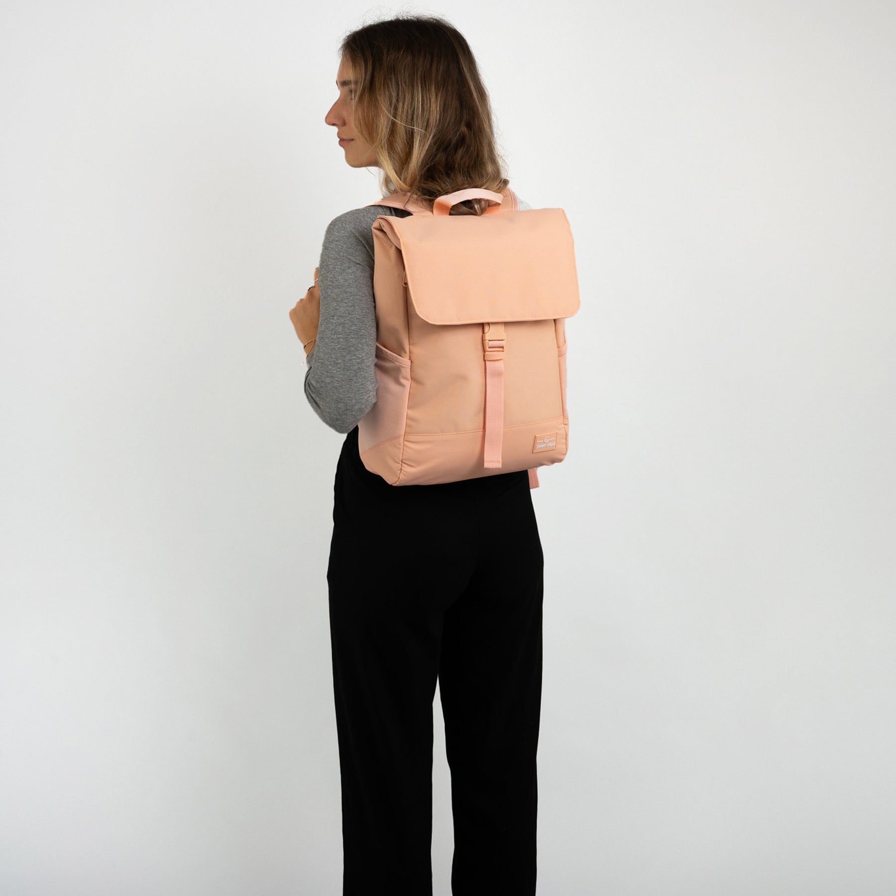 Frau von hinten mit peachfarbenem Rucksack 'Mika', graues Oberteil, schwarze Hose