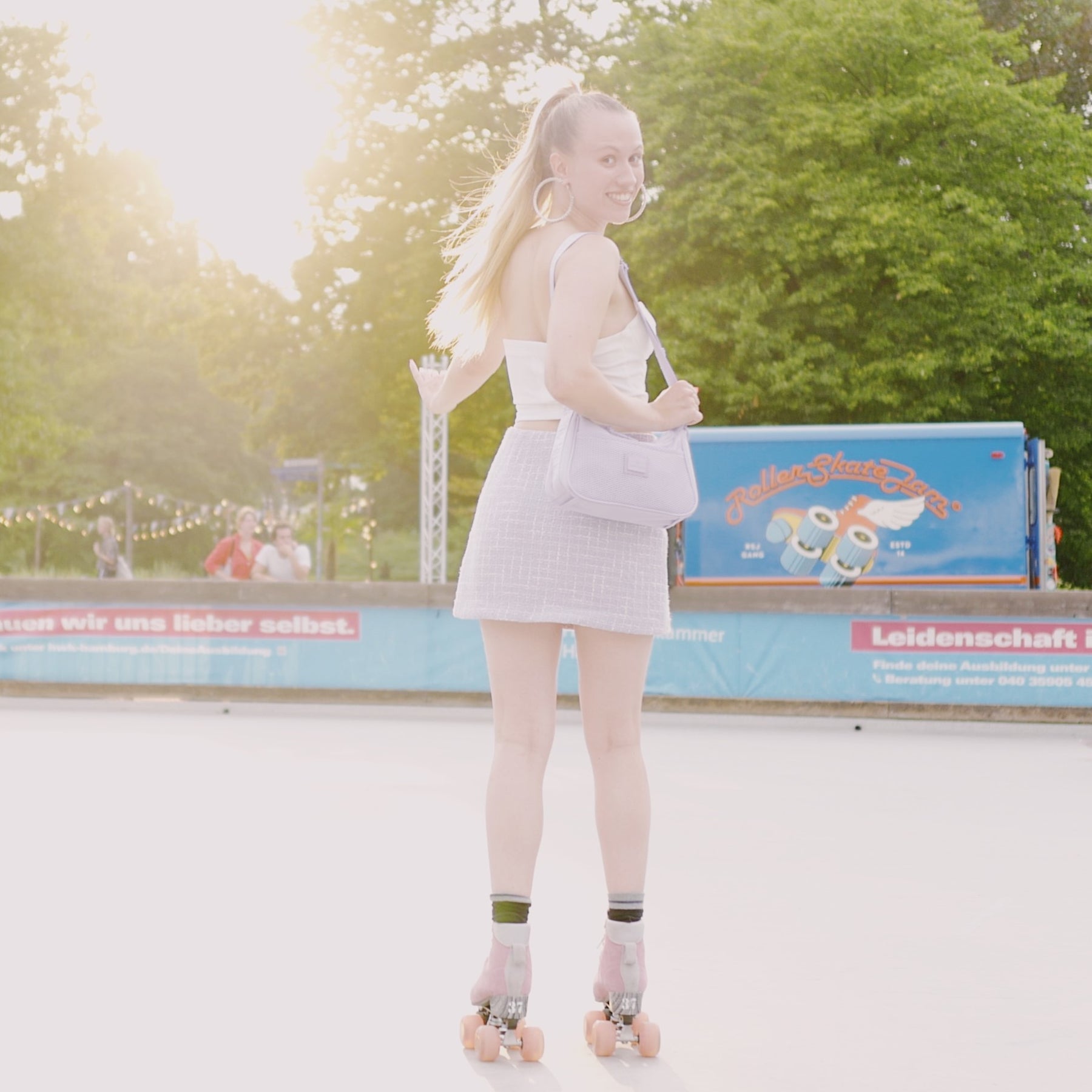 Frau auf Rollschuhen mit lilafarbener Handtasche 'Maddy' von Johnny Urban und weißem Outfit bei Sonnenlicht im Park