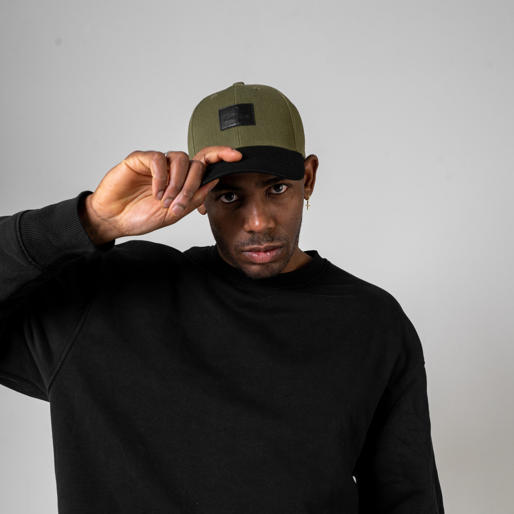 Mann trägt grün-schwarze Johnny Urban Cap 'Dean' und schwarzen Pullover, hebt die Kappe mit der Hand