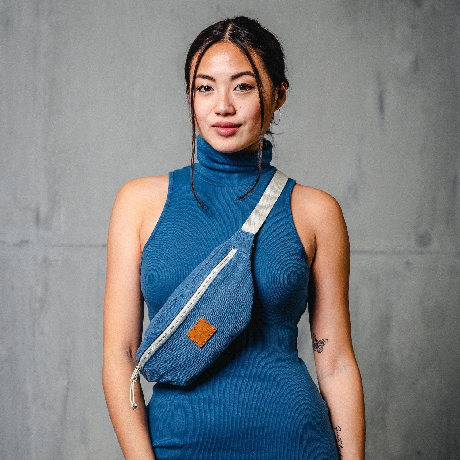 Frau trägt Bauchtasche ‚Toni‘ aus blauem Jeans-Denim mit weißem Reißverschluss und verstellbarem weißen Gurt quer am Oberkörper