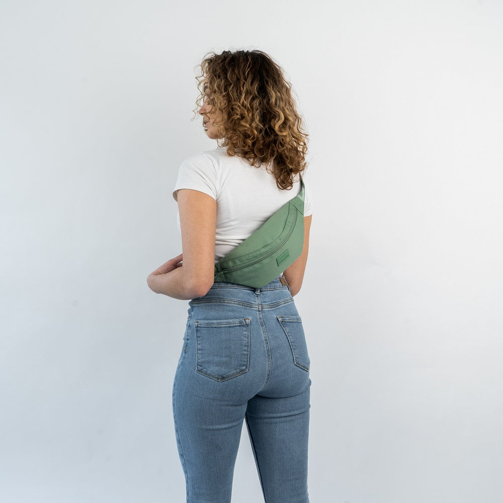 Frau mit weißen T-Shirt und blauen Jeans trägt die Bauchtasche 'Erik Small' in Salbeigrün über den Rücken