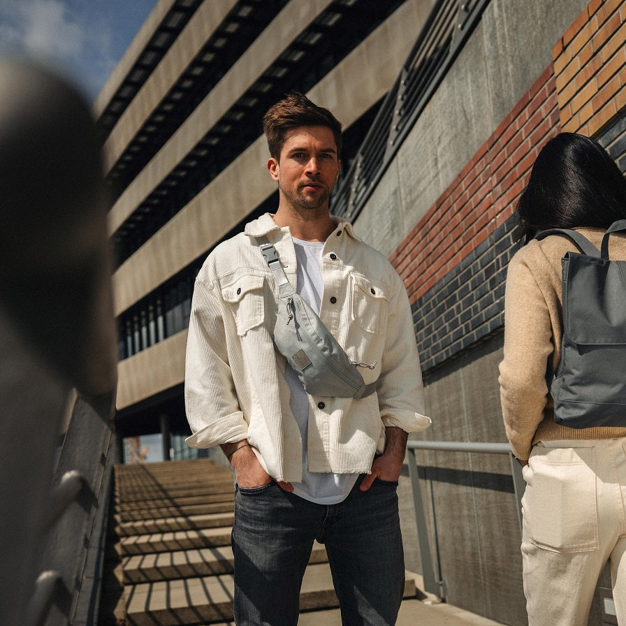 Mann trägt graue Bauchtasche 'Erik Small' quer am Oberkörper, weiße Jacke, weiße T-Shirt, schwarze Jeans