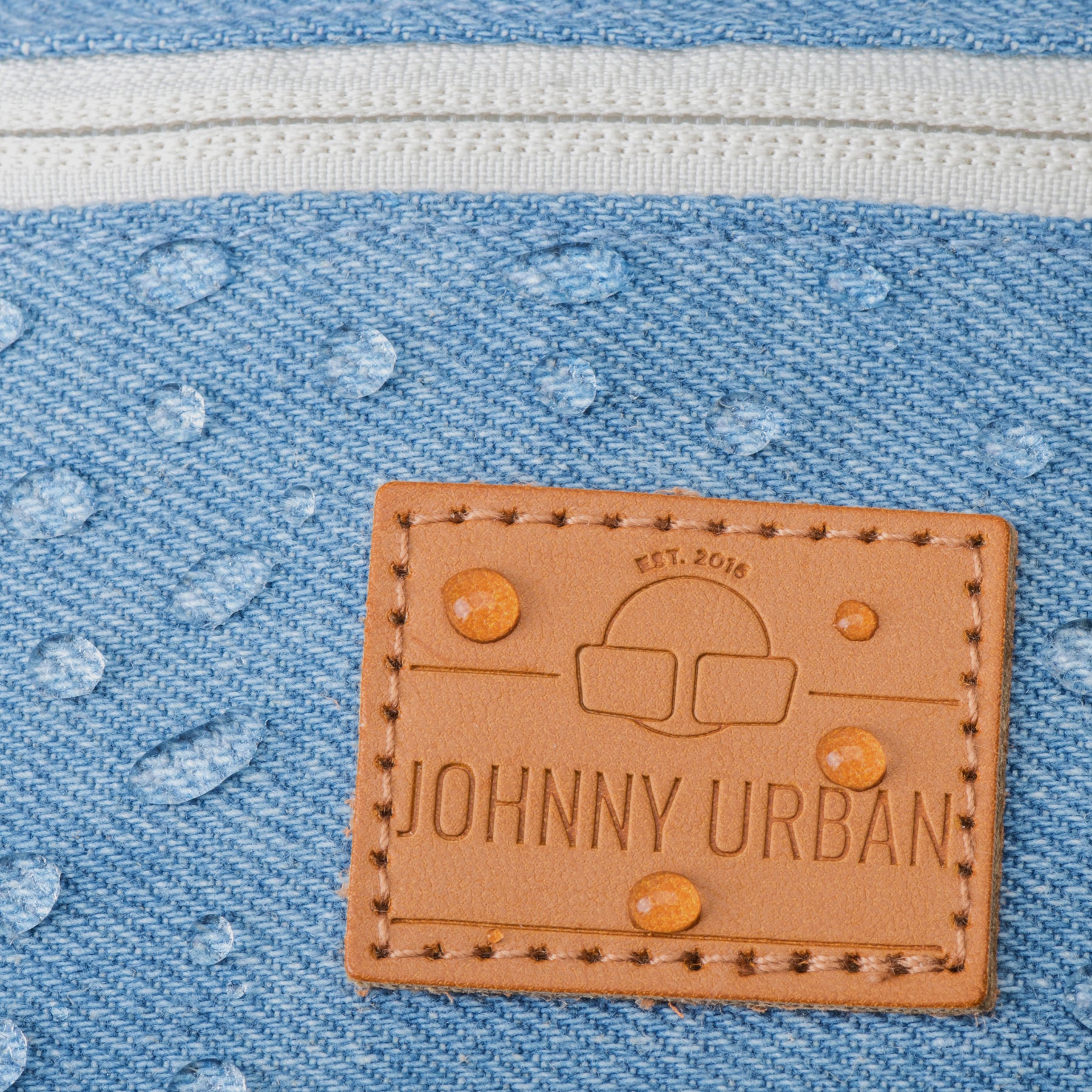 Nahaufnahme der wasserabweisenden blauen Jeans-Denim-Oberfläche der Bauchtasche 'Toni' von Johnny Urban mit braunem Markenlogo
