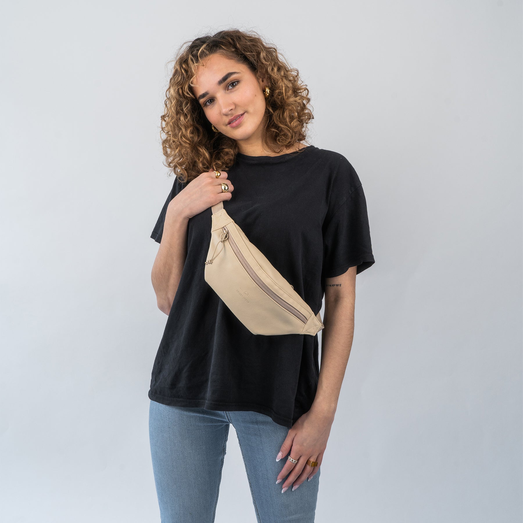 Frau trägt beige Bauchtasche 'Toni' aus Kunstleder über der Schulter zu schwarzem T-Shirt und blauen Jeans