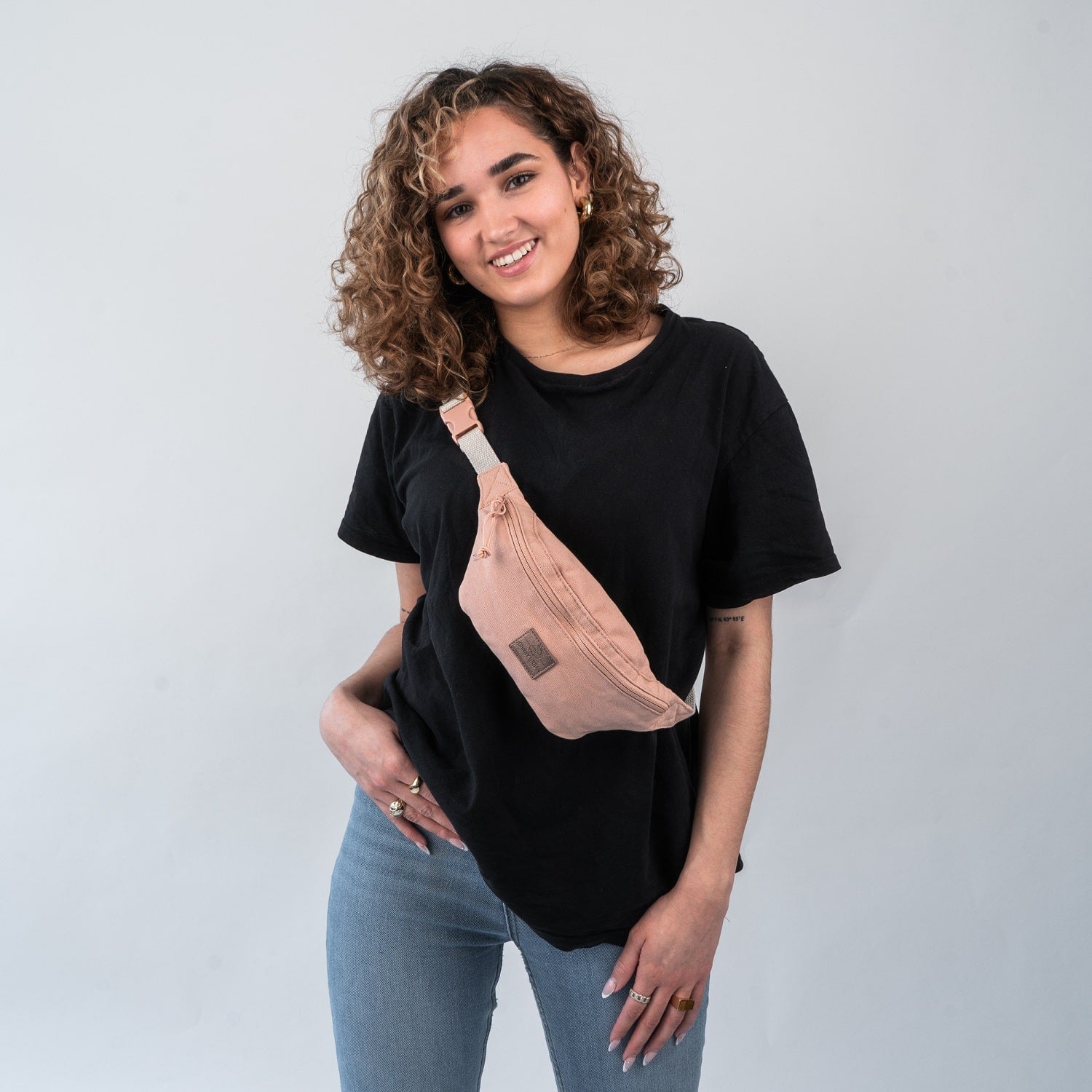 Frau trägt rosa Bauchtasche 'Toni' von Johnny Urban über schwarzem T-Shirt und blauen Jeans