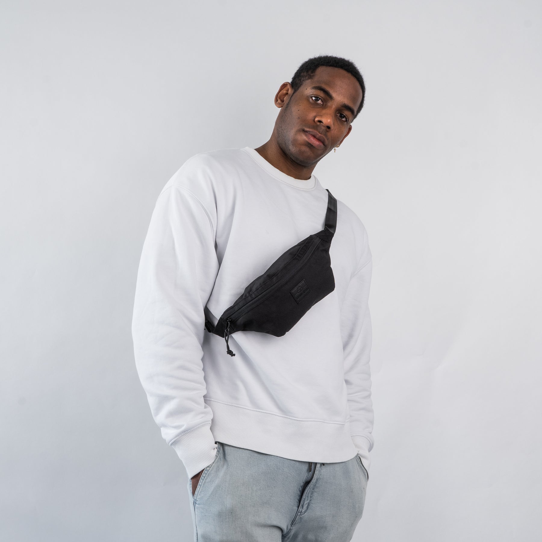 Mann trägt schwarze Johnny Urban Bauchtasche 'Erik Small' quer über der Brust mit weißem Pullover und Jeans