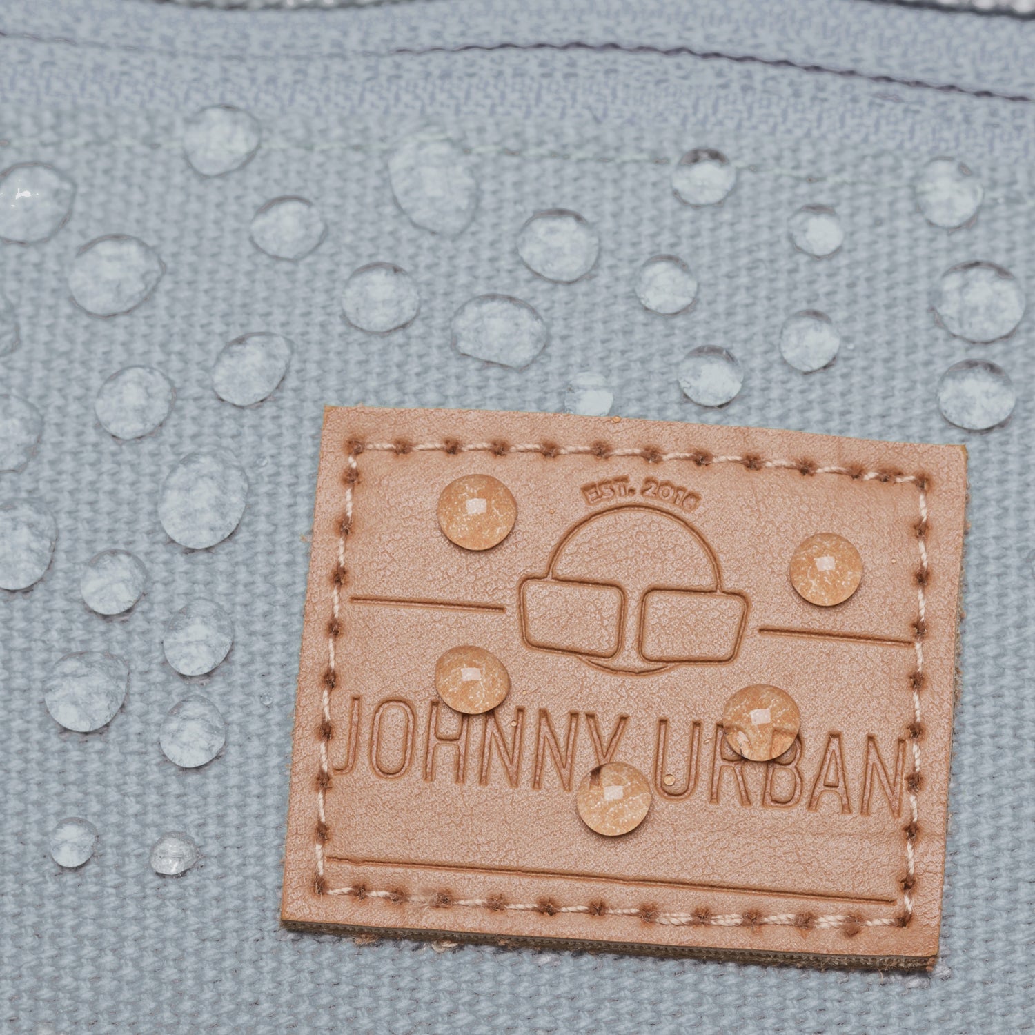 Wasserabweisender grauer Stoff mit braunem Johnny Urban Lederetikett und Wasserperlen