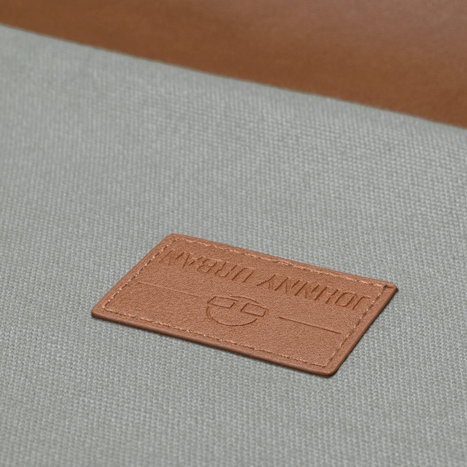 Nahaufnahme des braunen Lederlabels mit Prägung 'Johnny Urban' auf grauem Canvas des Turnbeutels 'Luke'
