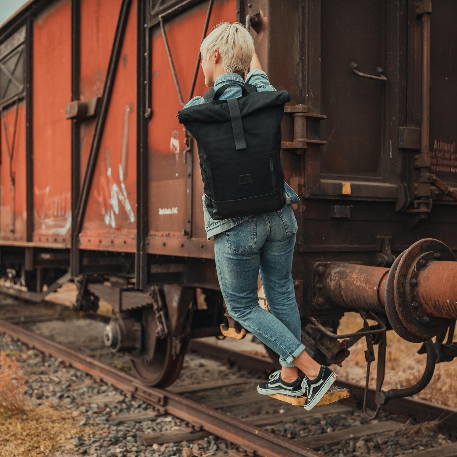 Person hängt an einem Lastwagen, trägt schwarzen Rolltop Rucksack Adam Large von Johnny Urban