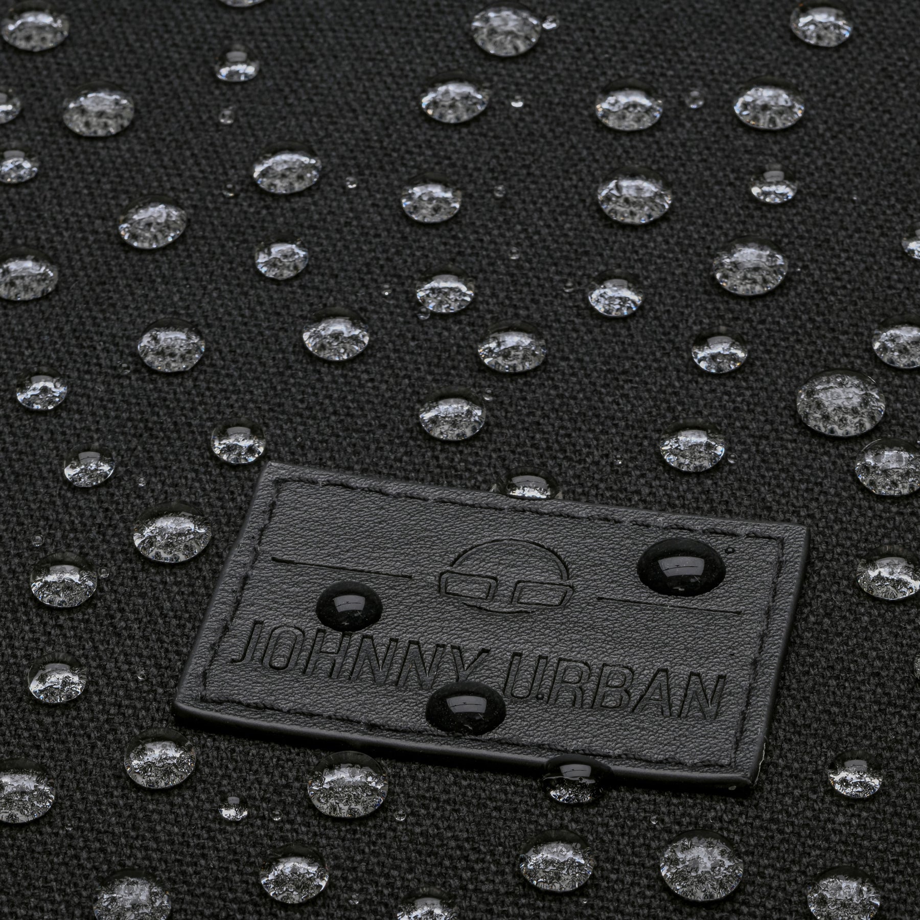Wasserabweisender schwarzer Canvas-Stoff mit Wasserperlen und Johnny Urban Logo aus schwarzem Leder