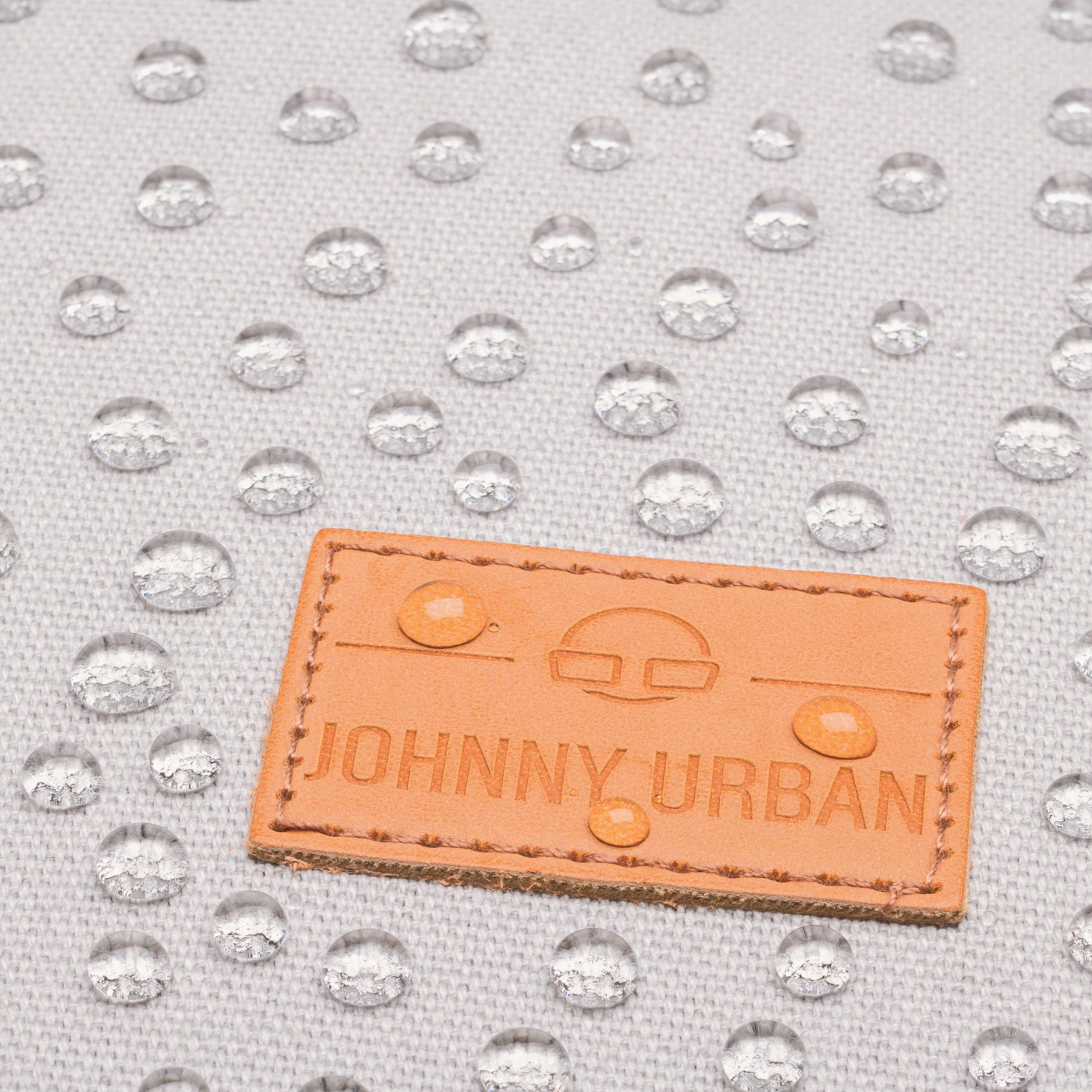 Wasserabweisendes graues Canvas-Material mit JOHNNY URBAN Lederetikett und Wassertropfen