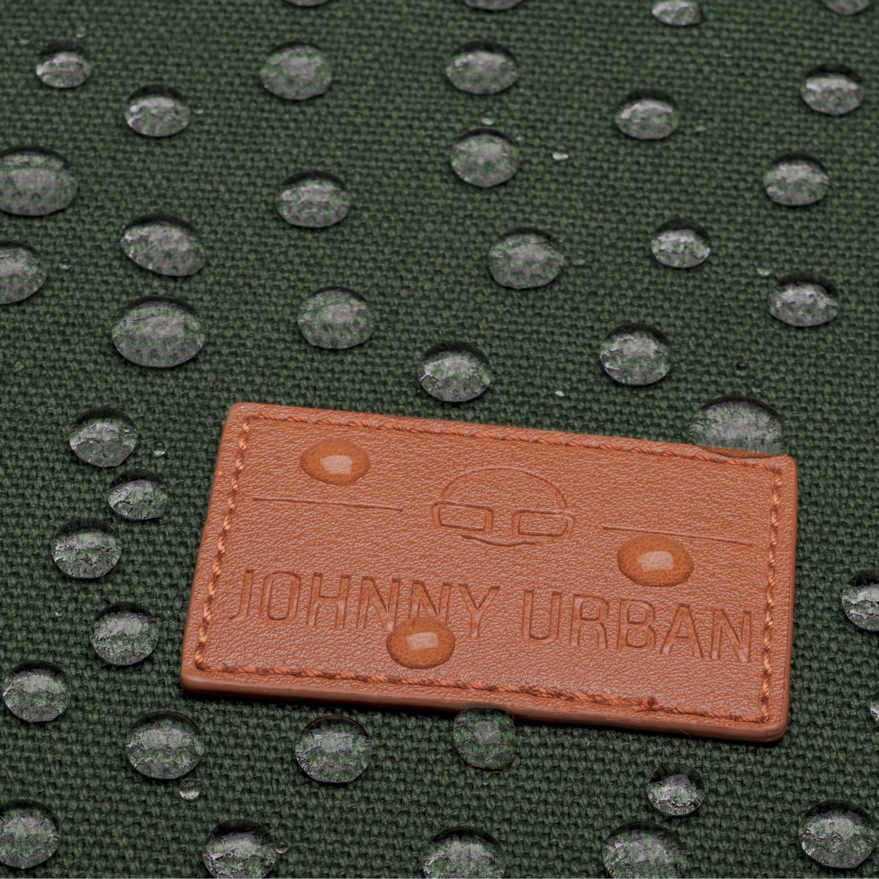 Wasserabweisendes grünes Canvas-Material mit braunem Johnny Urban Lederetikett und Wassertropfen