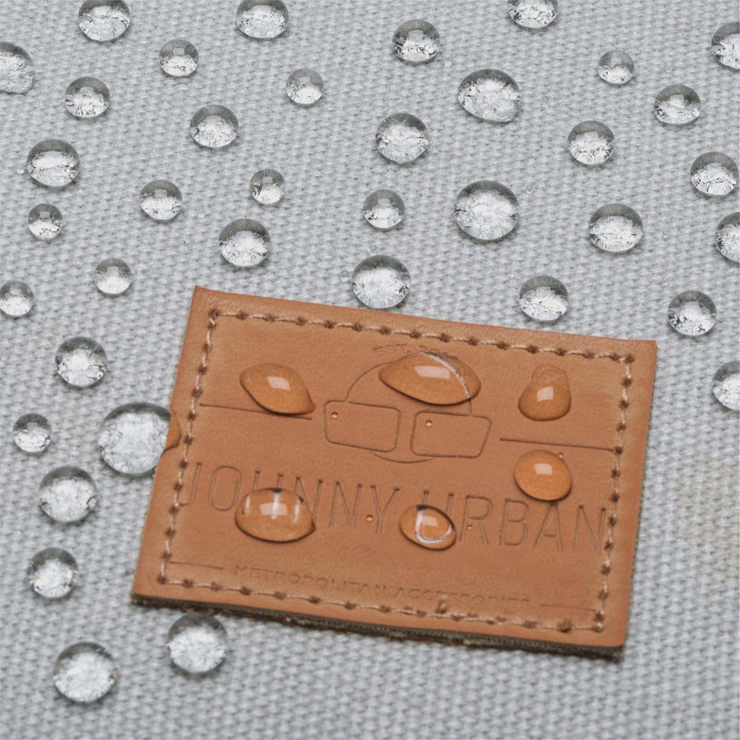 Wasserabweisendes graues Canvas-Material mit Johnny Urban Lederetikett und Wassertropfen darauf