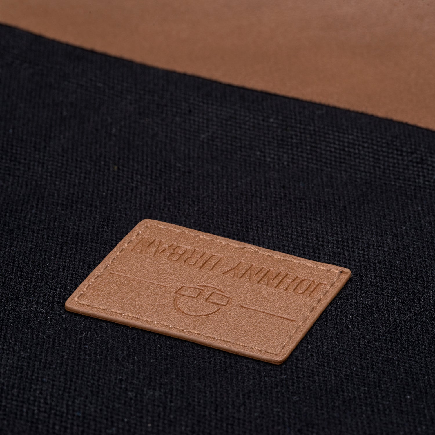 Braunes Lederetikett mit geprägtem 'Johnny Urban' Schriftzug auf schwarzem Canvas Turnbeutel