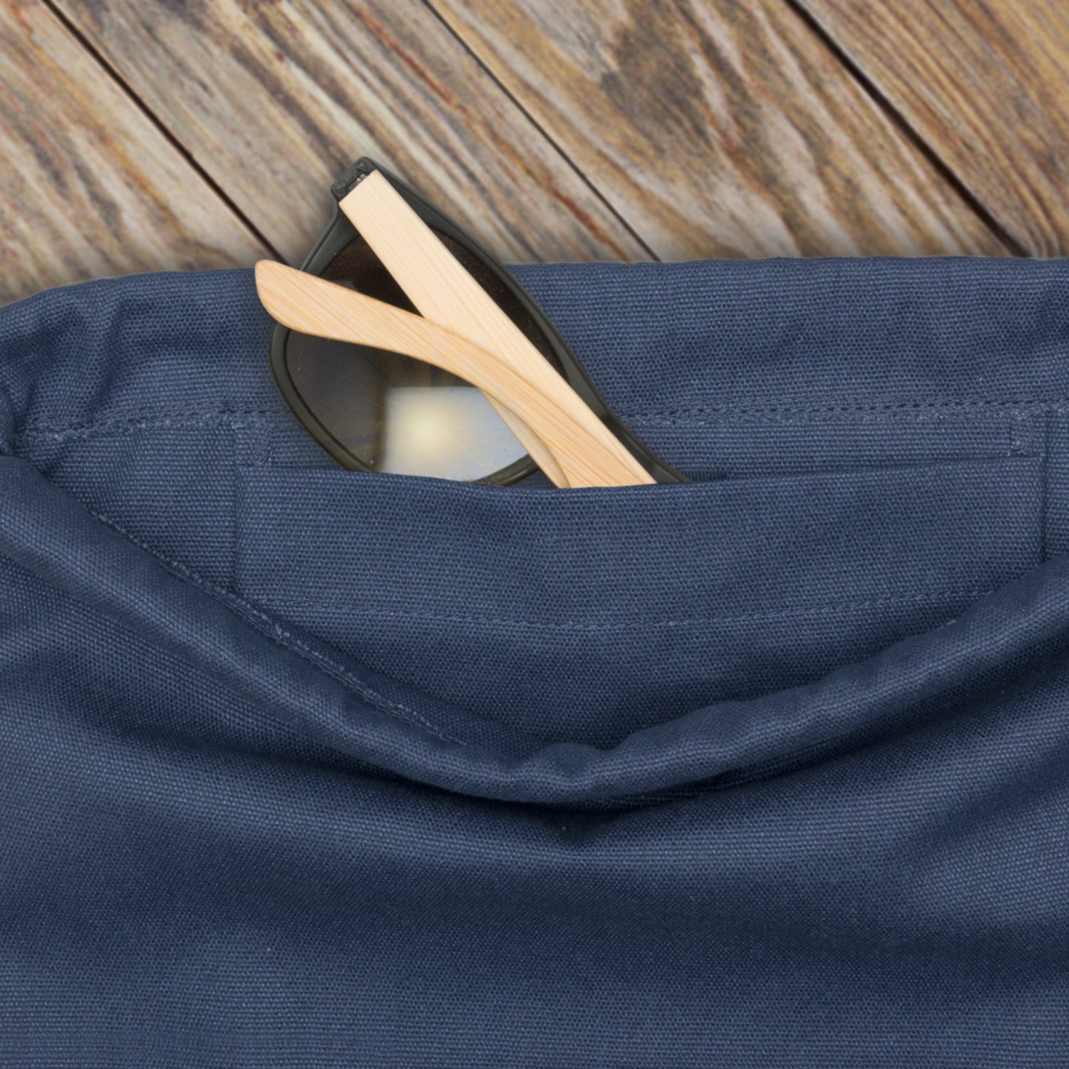 Blauer Canvas-Turnbeutel 'Luke' mit einer Außentasche, in der eine Sonnenbrille mit hellen Bügeln steckt