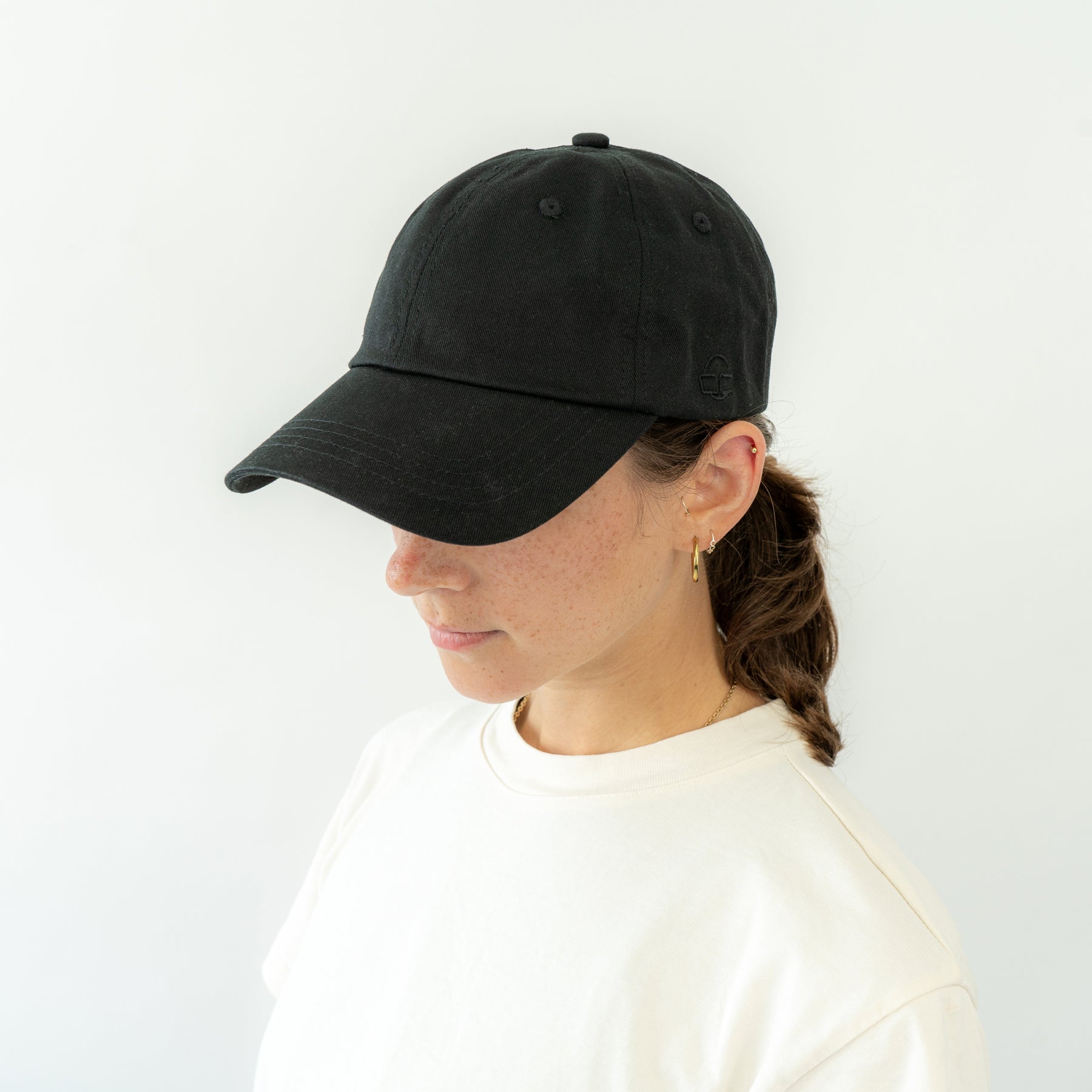 Frau trägt schwarze Canvas-Kappe 'Jen' mit gebogenem Schirm und weißen Oberteil