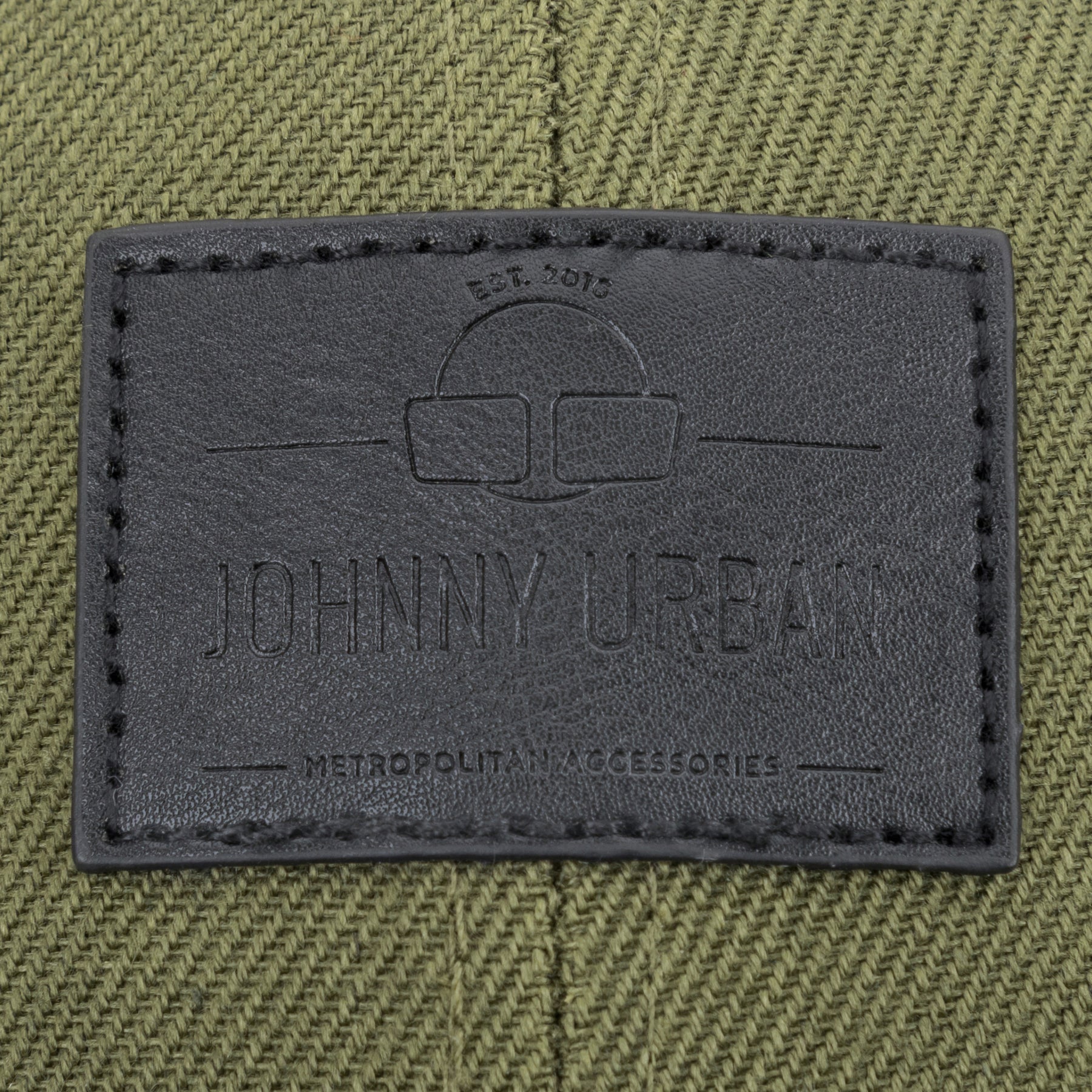 Schwarzes Lederetikett mit Johnny Urban Logo und Text auf grün-schwarzem Canvas-Material.