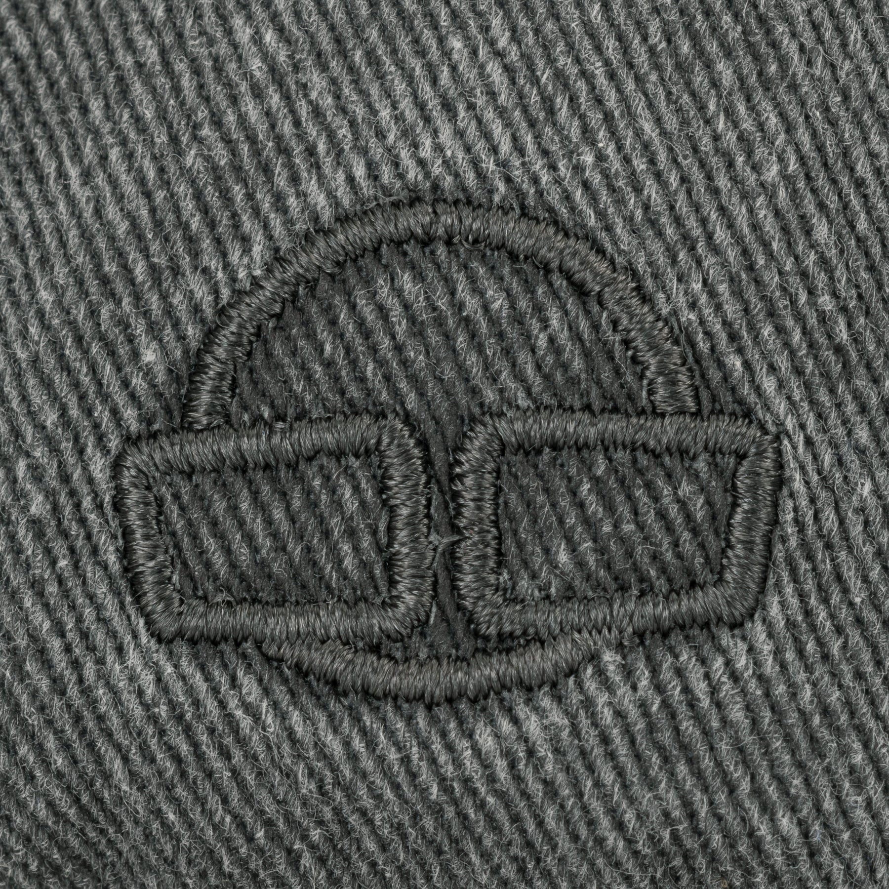 Nahaufnahme des schwarzen gestickten Logos auf grauem Canvas-Gewebe der Cap 'Dave' von Johnny Urban