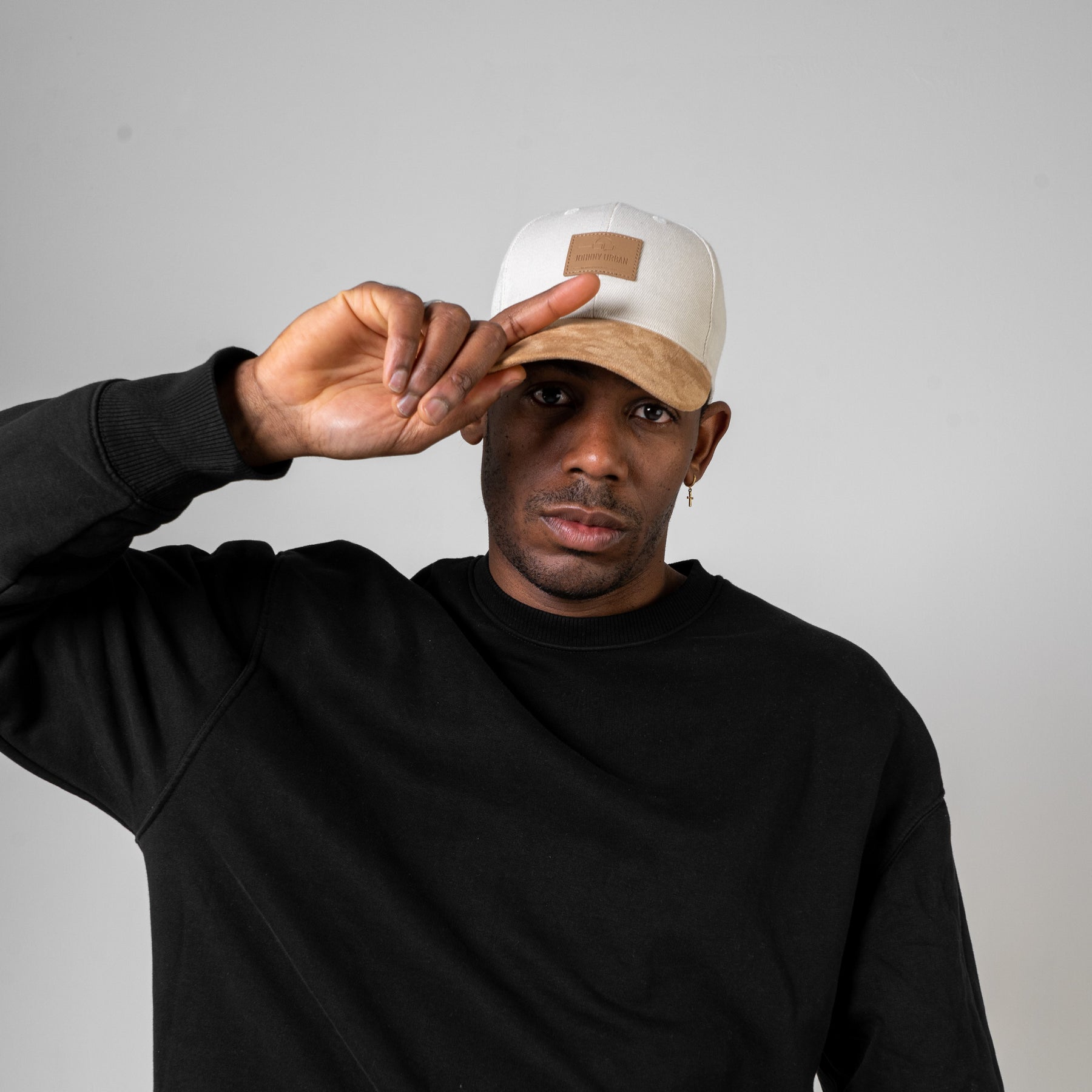 Mann trägt beige Cap 'Dean' mit gebogenem Schirm und braunem Logo, schwarzes Sweatshirt