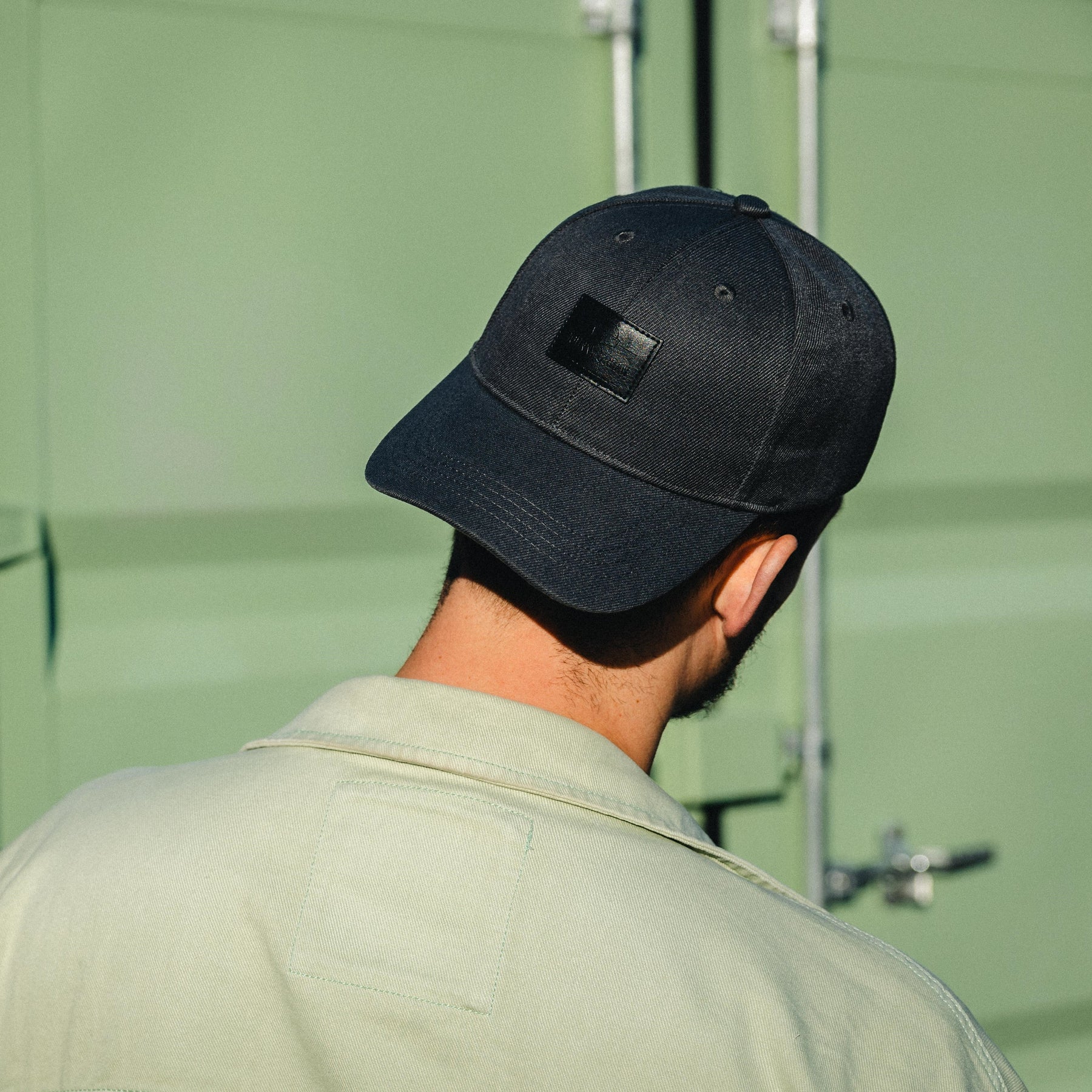 Schwarze, gewölbte Herren-Cap 'Dean' mit Lederpatch auf dem Kopf eines Mannes von hinten