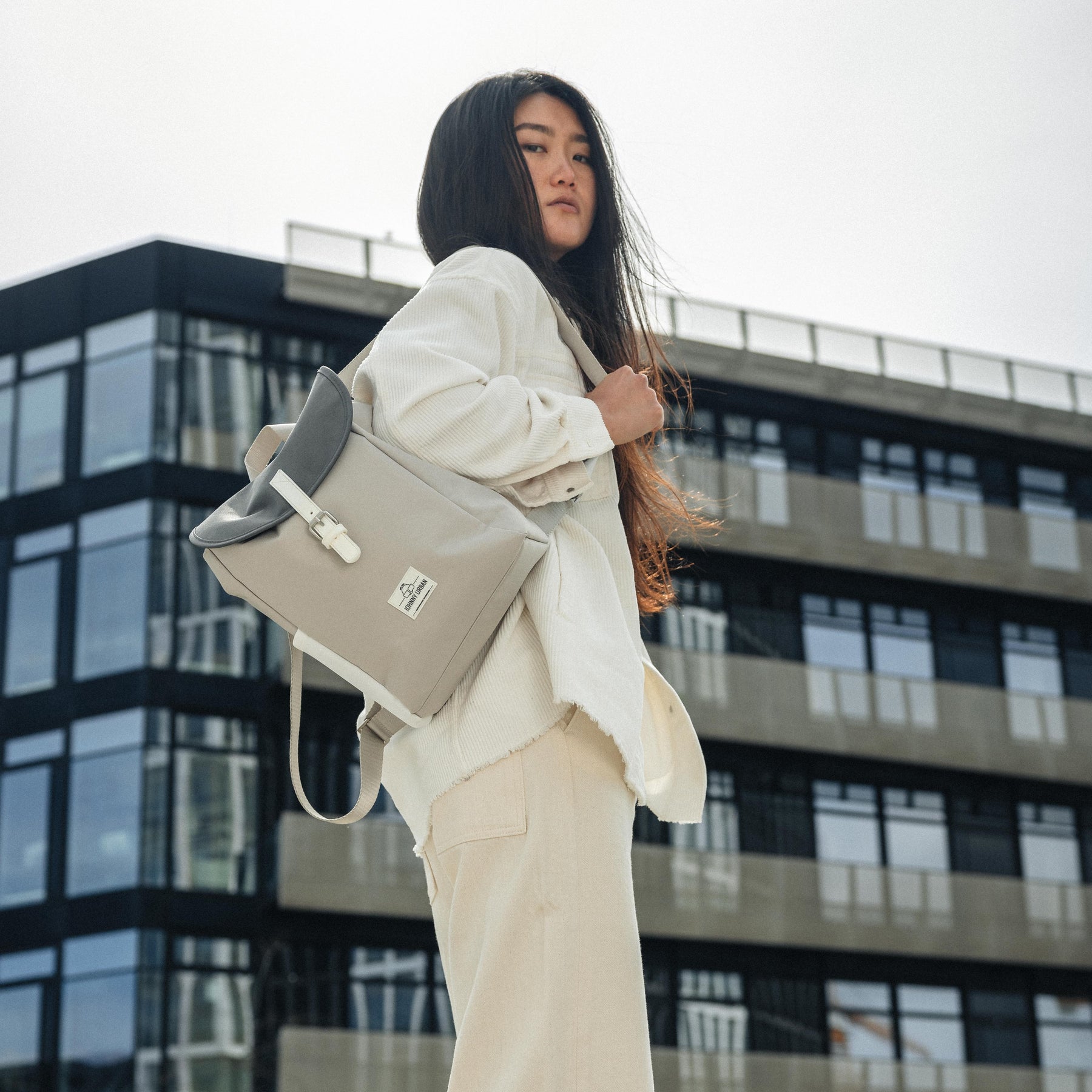 Frau mit hellem Rucksack 'Romy' von Johnny Urban, helle Kleidung, urbanes Gebäude im Hintergrund
