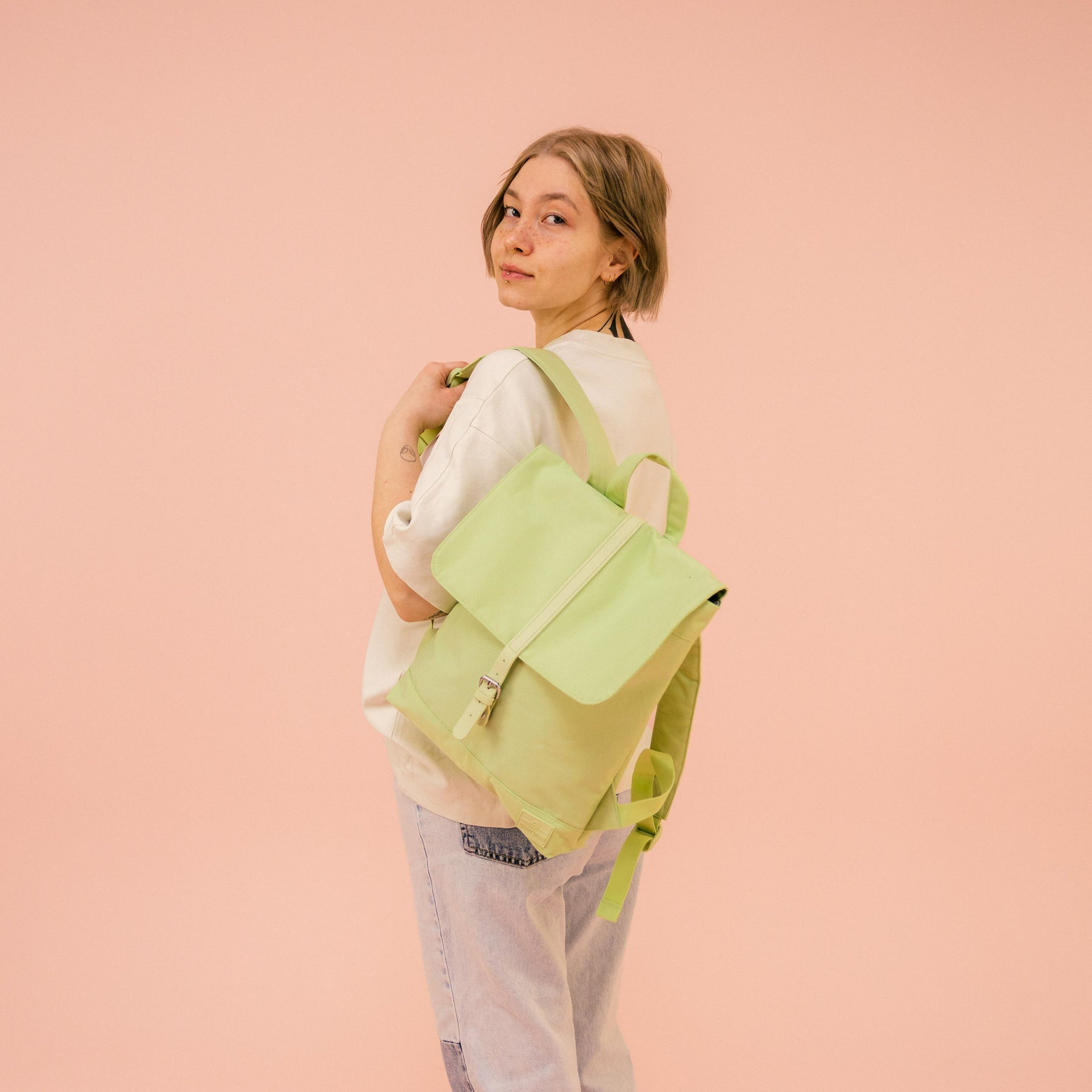 Frau trägt limegrünen Damen-Rucksack 'Mia' von Johnny Urban über dem Schulter, beige Sweatshirt, helle Jeans