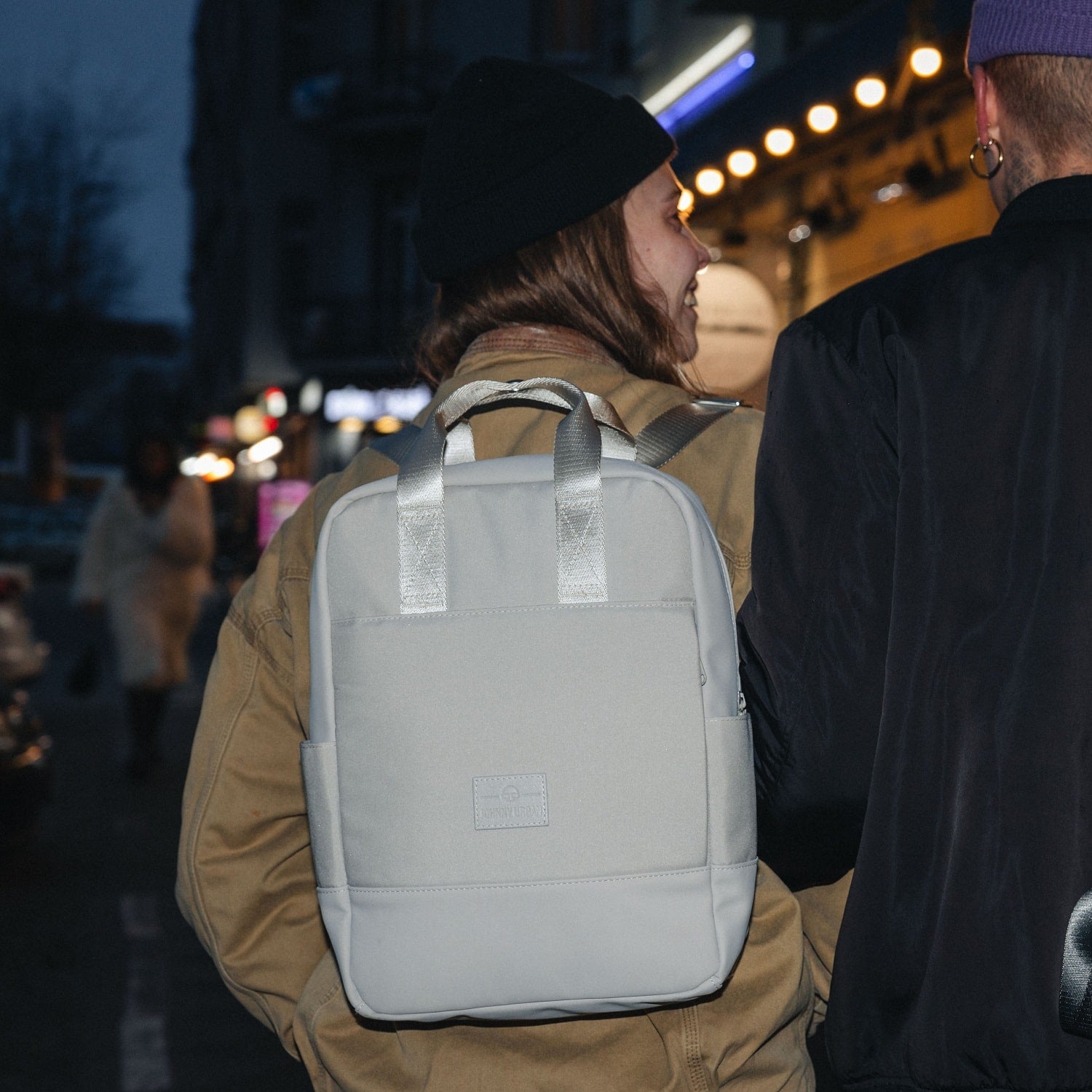 Frau trägt beigen Damenrucksack Jona Medium von Johnny Urban auf Rücken in urbaner Nachtumgebung