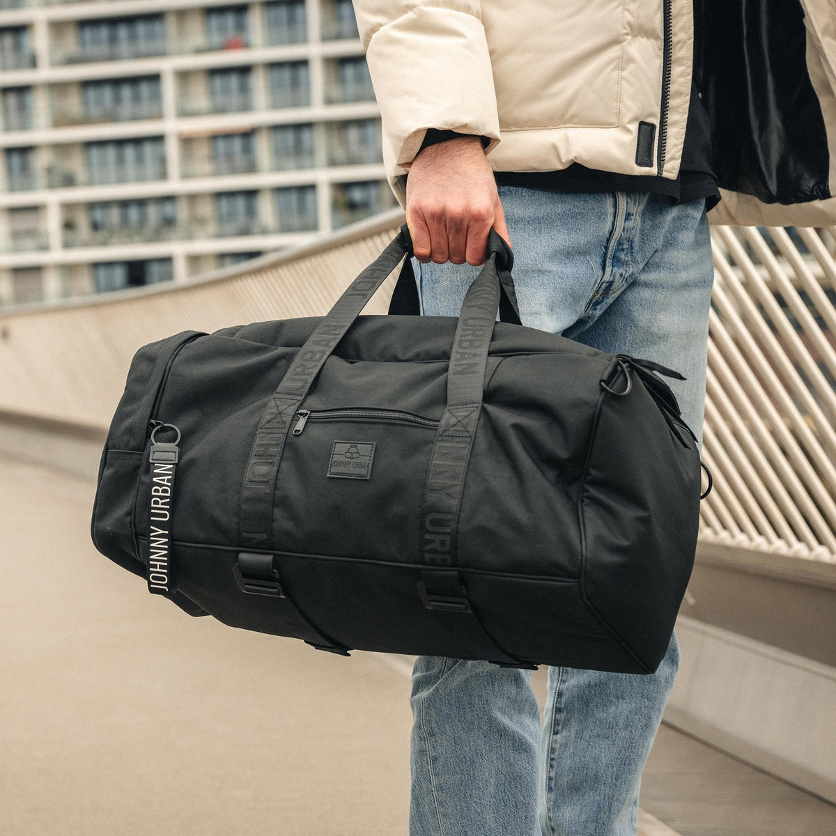 Schwarze Johnny Urban Duffle Bag 'Colin' aus robustem Material, getragen von Mann in beiger Jacke und Jeans