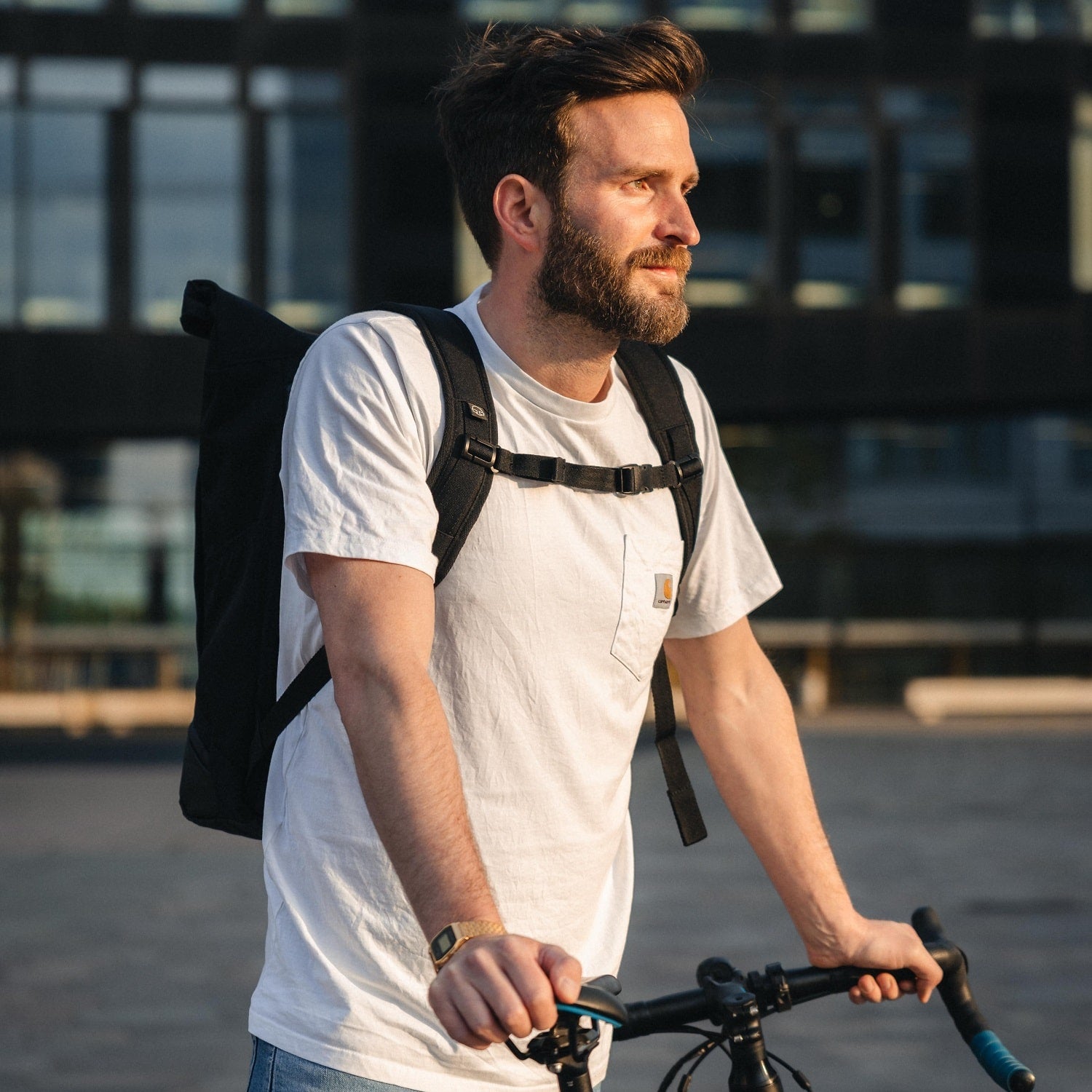 Mann trägt schwarzen Rolltop Rucksack 'Allen Large' von Johnny Urban und hält Fahrradlenker