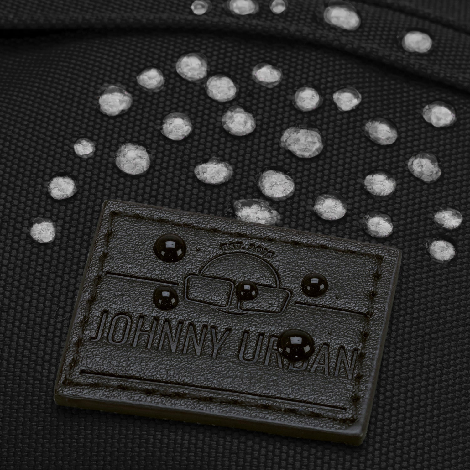 Nahaufnahme der wasserabweisenden schwarzen Bauchtasche 'Tom' von Johnny Urban mit sichtbaren Wassertropfen auf dem Material und geprägtem Logo